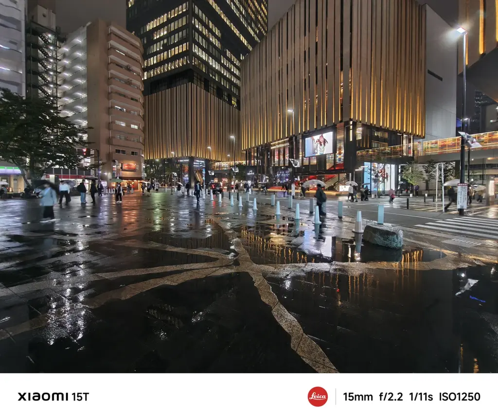 Xiaomi 15Tの超広角カメラで撮影した広場の夜景。雨に濡れた地面にネオンが反射し、Leica Authenticらしい深みのある描写