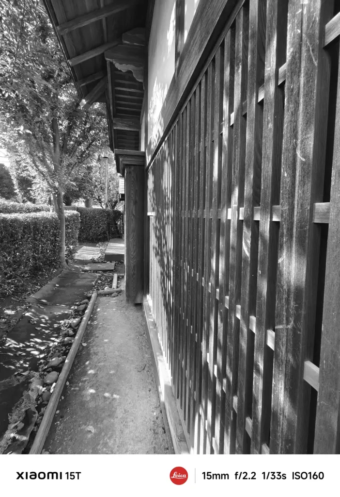Xiaomi 15TのLeicaモノクロフィルターで撮影した日本家屋の外壁。木漏れ日が格子に落ち、陰影豊かな情景を描き出す