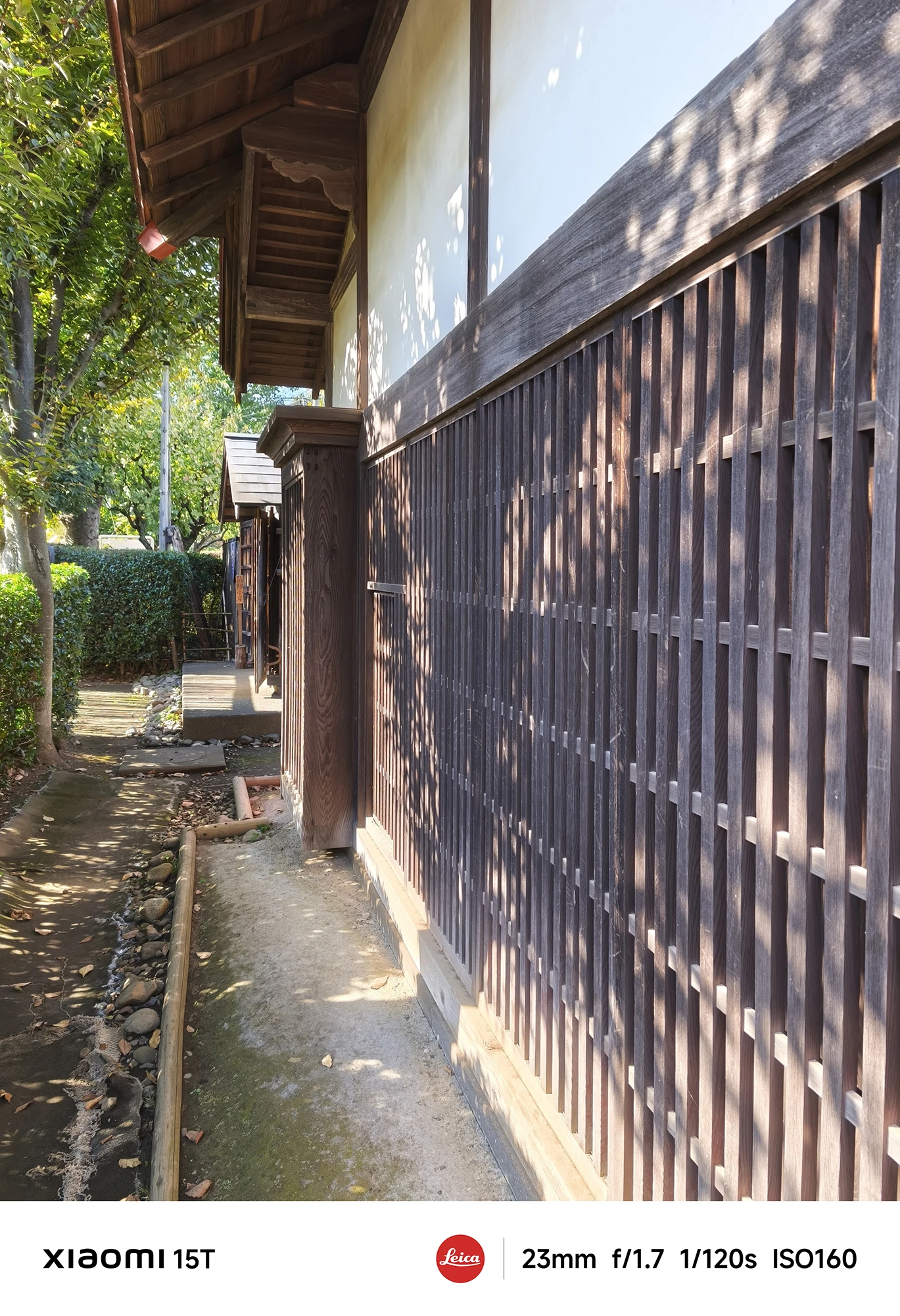 Xiaomi 15Tのメインカメラで撮影した木格子の外壁と細い通路。建築の陰影と自然光のコントラストが際立つ日本家屋の一枚