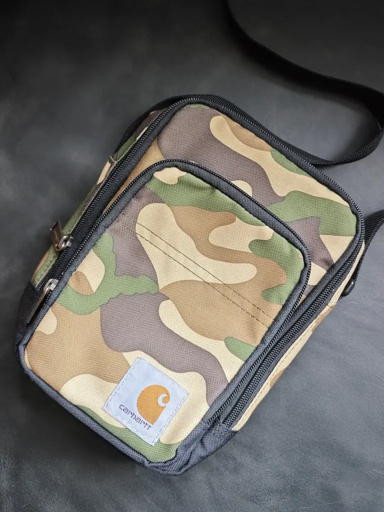 Carhartt（カーハート）のロゴパッチが付いたカモフラージュ（迷彩）柄の小型ショルダーバッグ（サコッシュ）。コンパクトで複数のジッパー付きポケットがある。