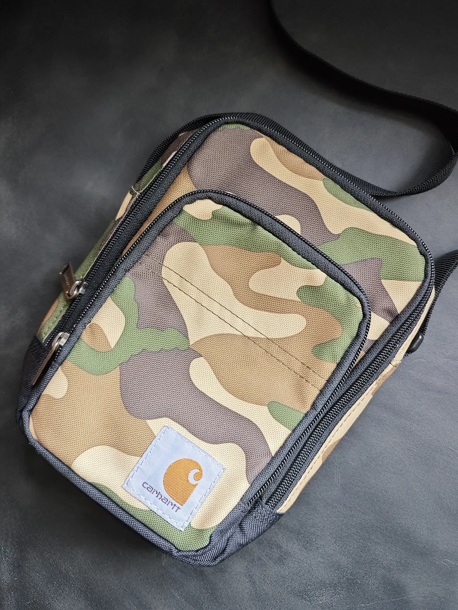 Carhartt(カーハート)のロゴパッチが付いたカモフラージュ(迷彩)柄の小型ショルダーバッグ(サコッシュ)。コンパクトで複数のジッパー付きポケットがある。