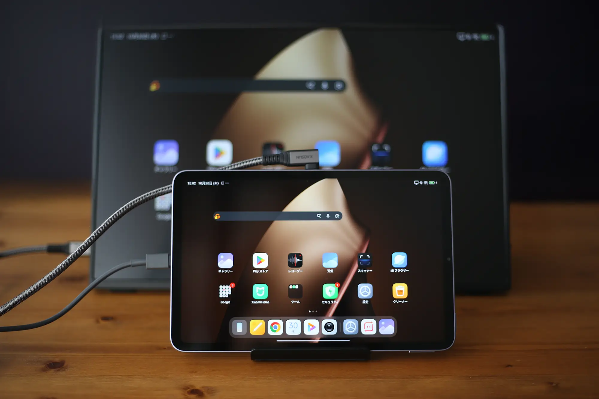 タブレットを外部モニターに接続し、画面をミラーリングしている様子。USB Type-Cケーブル(またはHDMIアダプター)で大画面に出力され、ホーム画面とアプリが表示されている。