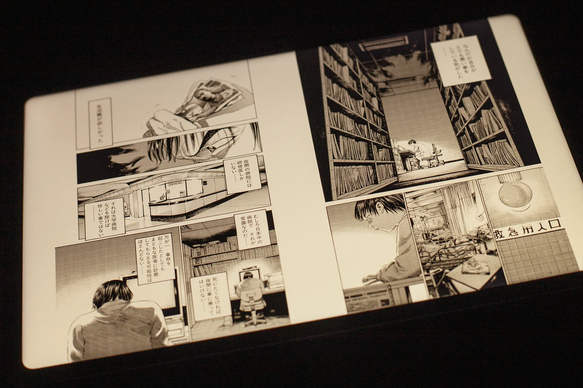 電子書籍リーダー(タブレット)でマンガを見開き表示している読書画面。モノクロの複雑なコマ割りと、書棚や病院のような室内背景が詳細に描かれている。