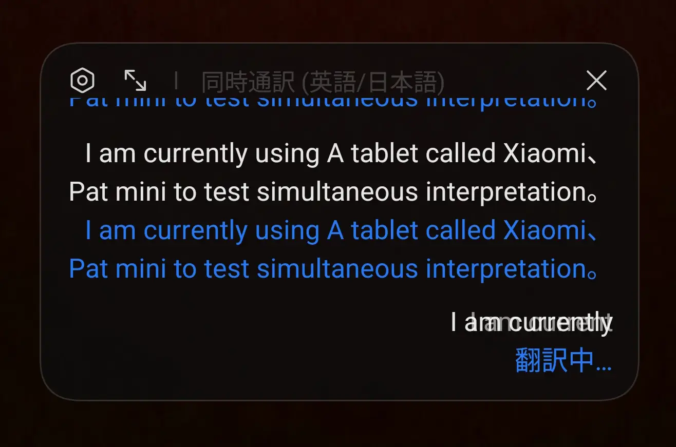 スマートフォン(タブレット)の「同時通訳(英語/日本語)」機能の実行画面。英語の文章が翻訳処理中で、「翻訳中...」の表示と共にリアルタイム通訳機能を示している。