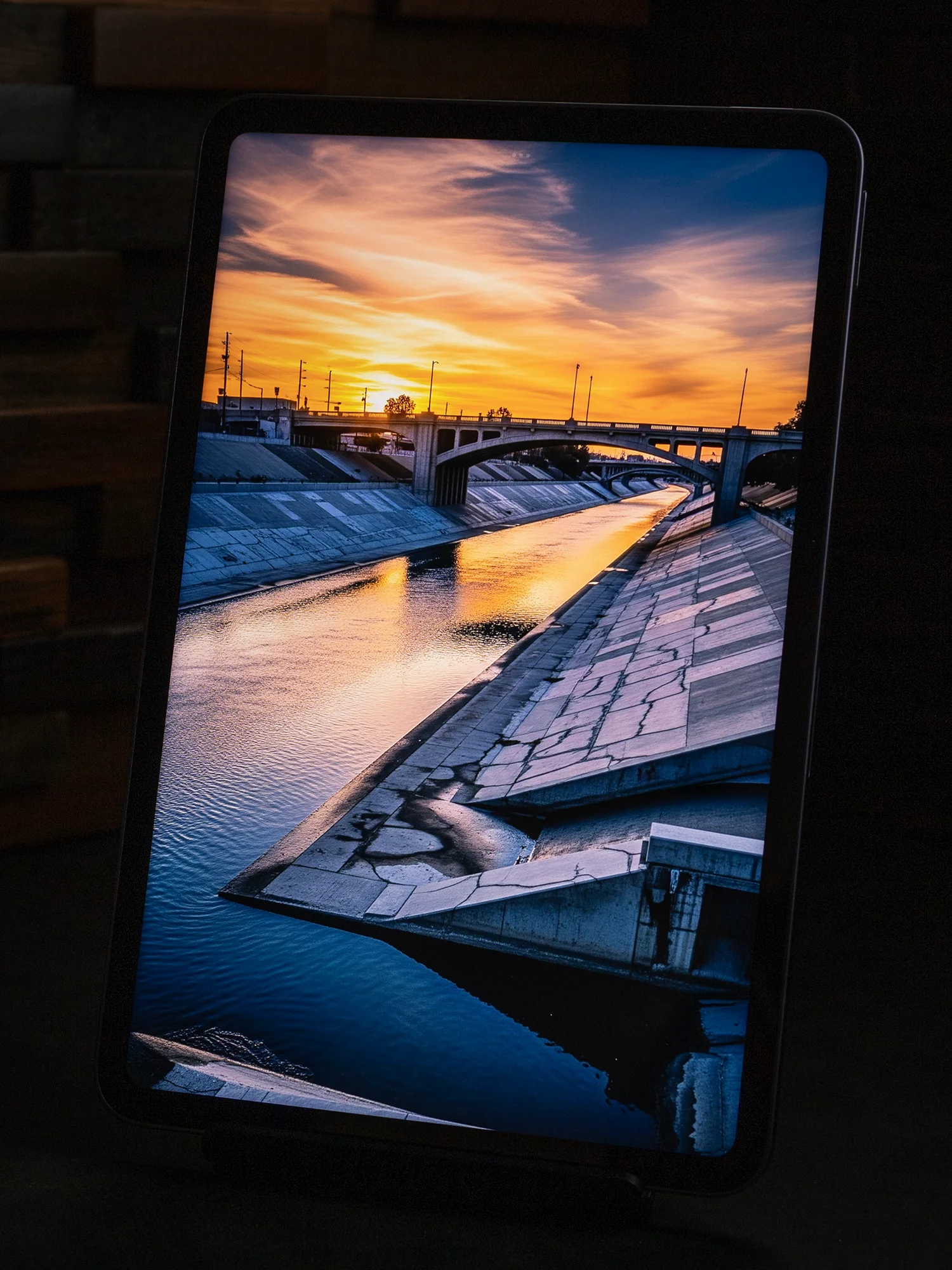 タブレットのディスプレイに表示された、夕焼け空とコンクリート護岸の水路(川)の風景写真。鮮やかなオレンジと青のコントラストが際立っている。