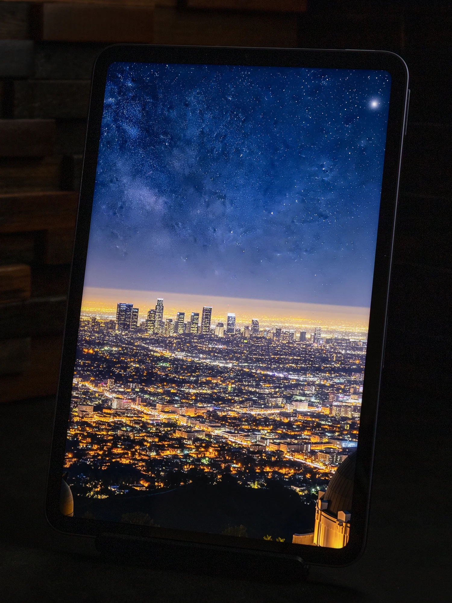 タブレットのディスプレイに表示された、夜の都市を見下ろす風景写真。地上の夜景と、満天の星空(天の川)のコントラストが際立っている。