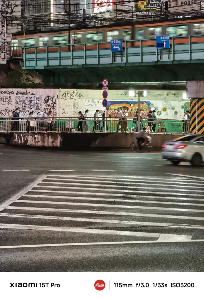 Xiaomi 15T Proで撮影した新宿駅付近の鉄道高架と交差点の夜景（115mm望遠、濡れた路面）