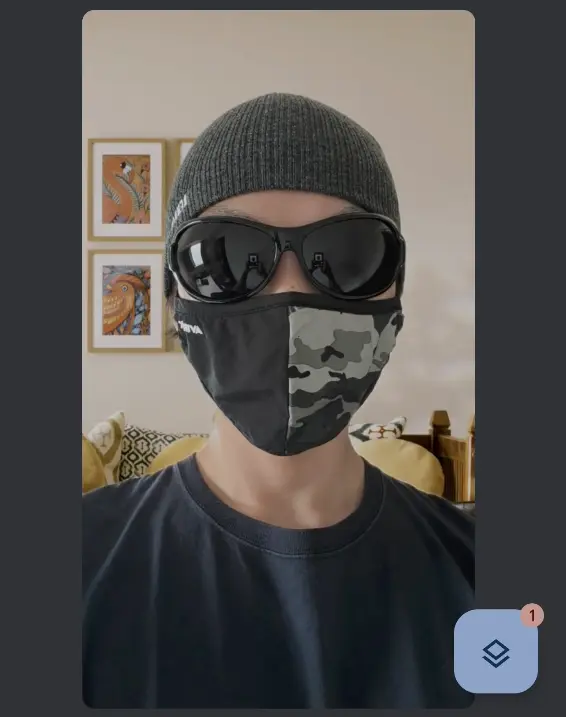 
画像をお送りいただきありがとうございます。 Google Meet使用時のスクリーンムービー（おそらくスクリーンショット）について、文字化けしないプレーンテキスト形式で代替テキストを作成します。 代替テキスト案（34枚目、Google Meetスクリーンショット）
Google Meetのビデオ通話画面のスクリーンショット。ニット帽、黒いサングラス、迷彩柄のマスクを着用した人物の顔が映っている。背景は自宅の一室で、壁に動物の絵画が飾られ、ソファにはクッションが置かれている。