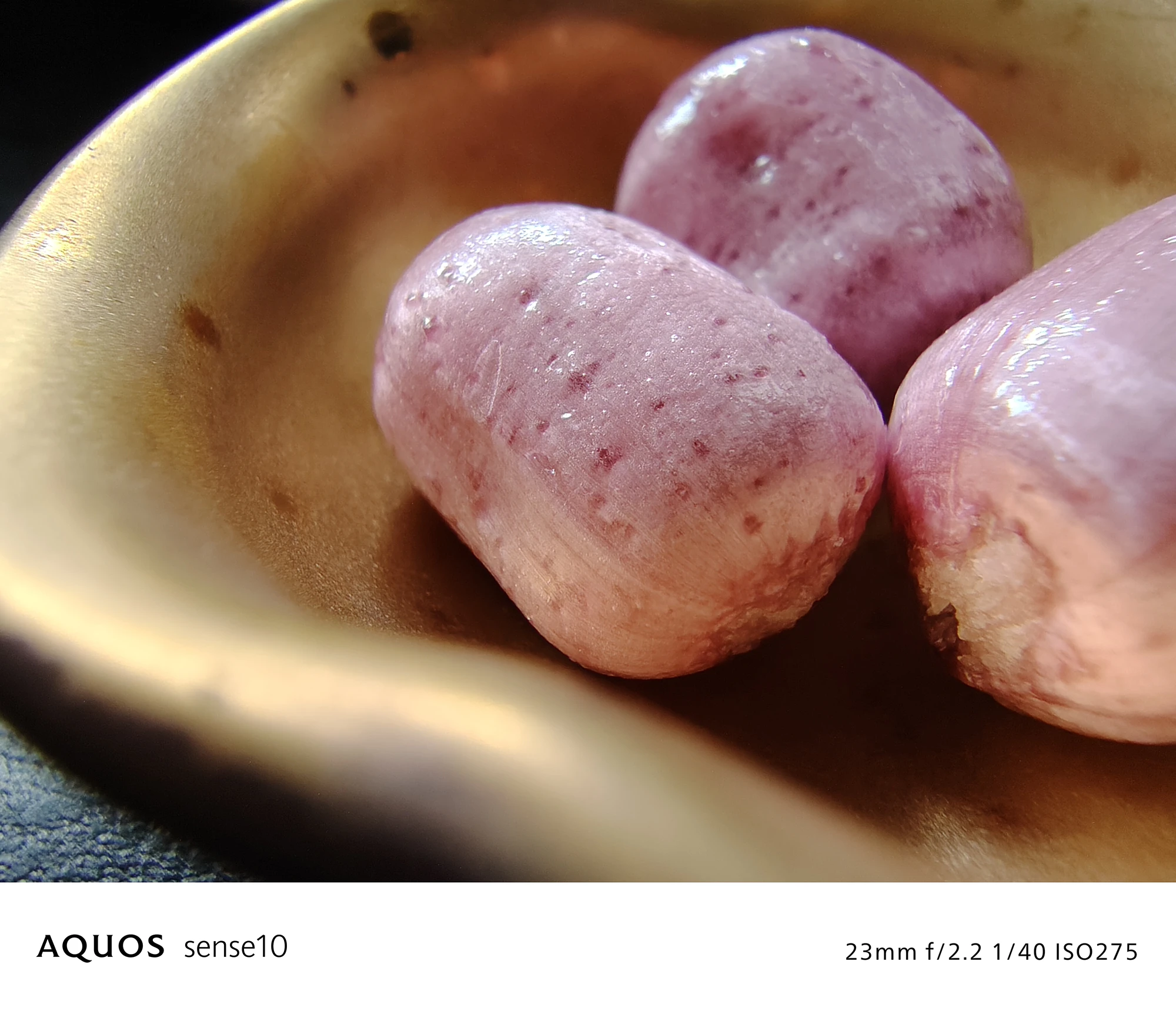 AQUOS sense10 撮影サンプル　銅色の皿に乗ったピンク色の飴（クローズアップ）	23mm f/2.2 1/40 ISO275