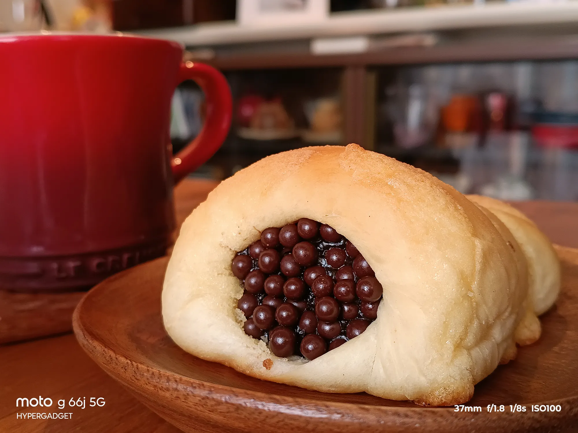moto g66j 5Gのカメラ作例：木皿に載ったチョコレートブレッドと赤いマグカップをクローズアップ。パンの質感とチョコレートのディテール、ボケ味をレビュー