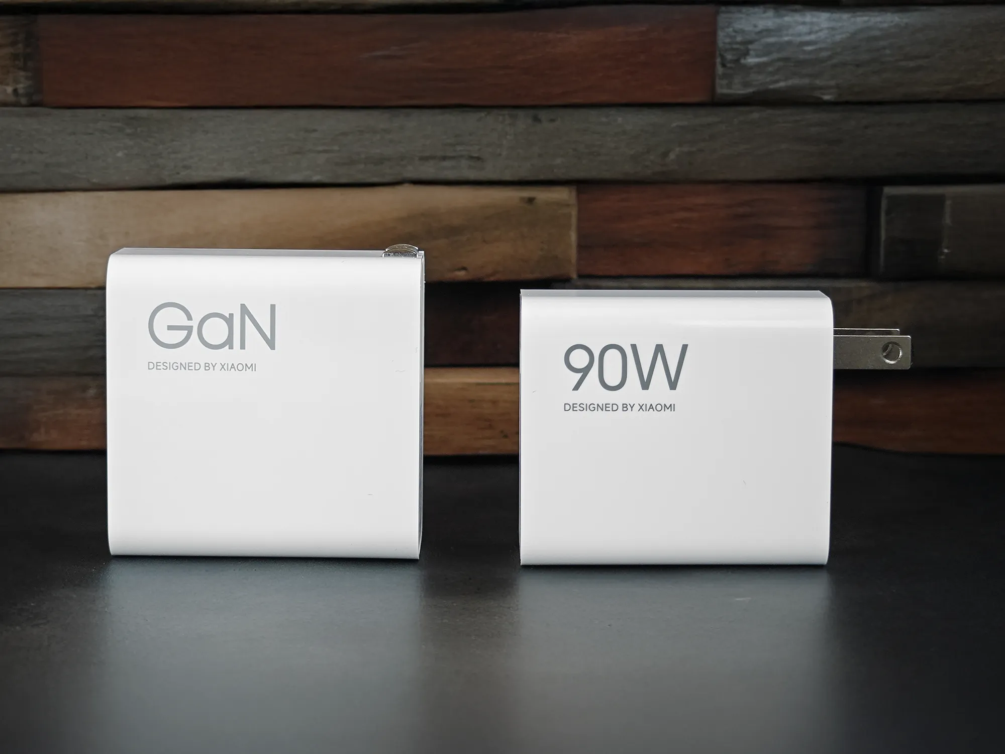 Xiaomi製の白い充電アダプター2種類を比較する写真。左側は「GaN DESIGNED BY XIAOMI」と書かれたGaN充電器。右側は「90W DESIGNED BY XIAOMI」と書かれた90W充電アダプター。背景は木目調の壁。