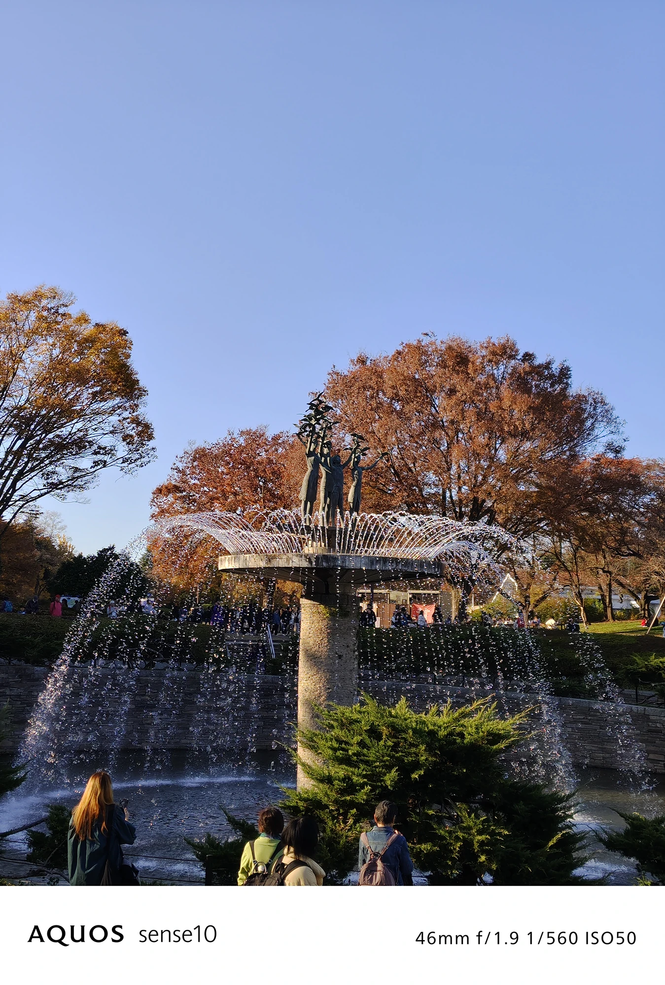 AQUOS sense10撮影サンプル：2倍ズームで捉えた公園の噴水と紅葉（f/1.9 ISO50）