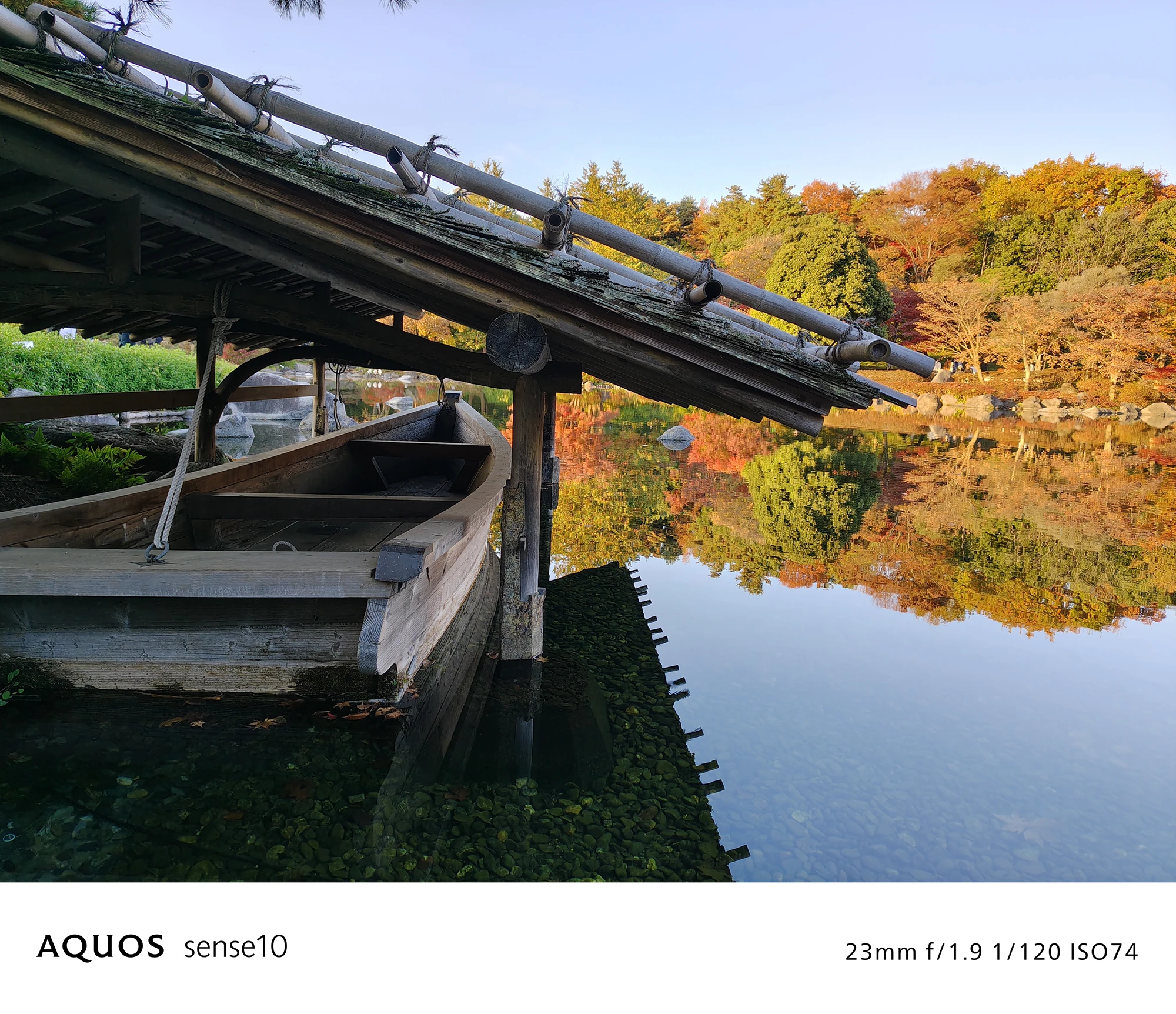 AQUOS sense10撮影サンプル：池のほとりの舟と紅葉のリフレクション（23mm f/1.9 ISO74）