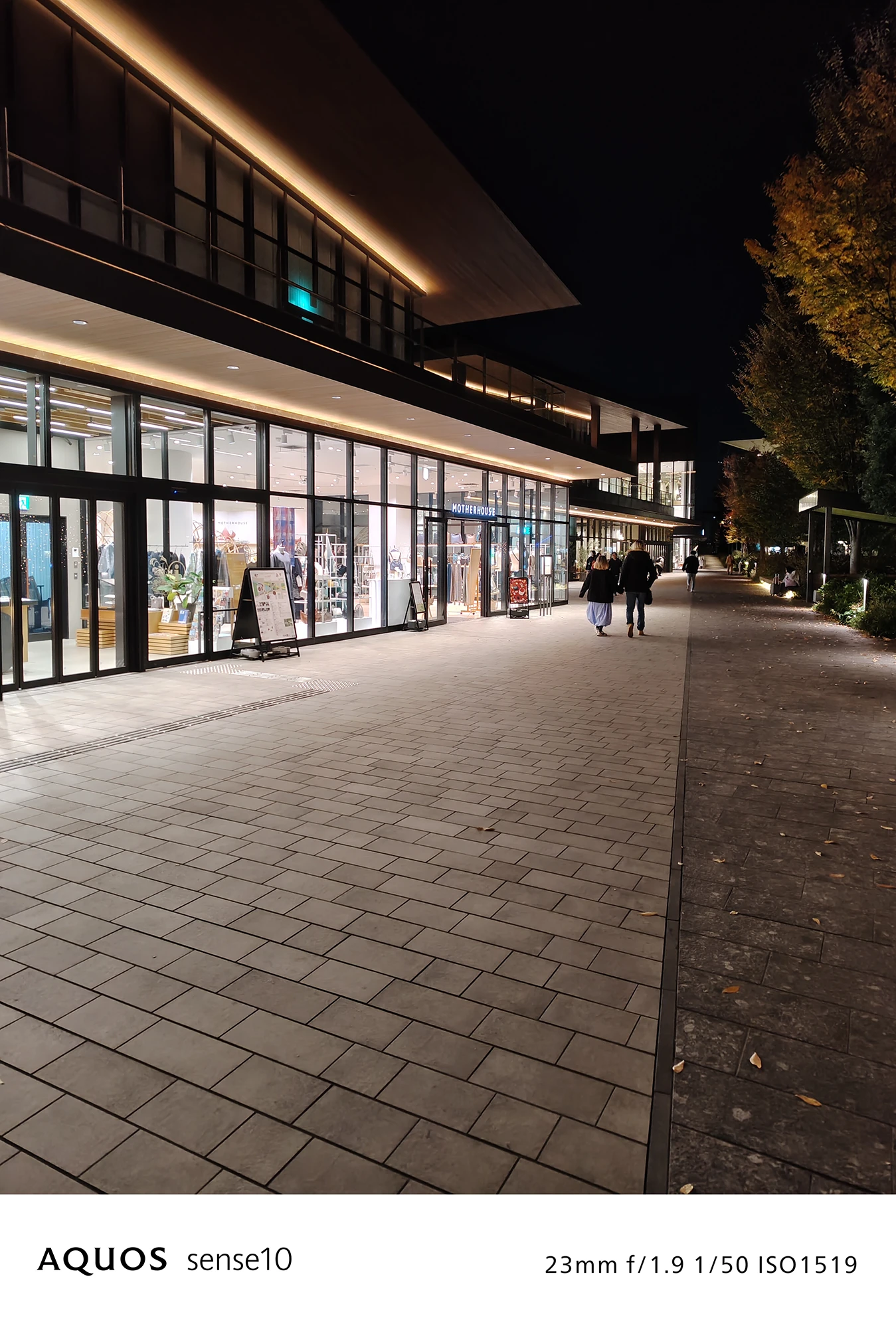 AQUOS sense10撮影サンプル：広角で捉えた**夜の商業施設と広々とした遊歩道**（f/1.9 ISO1519）