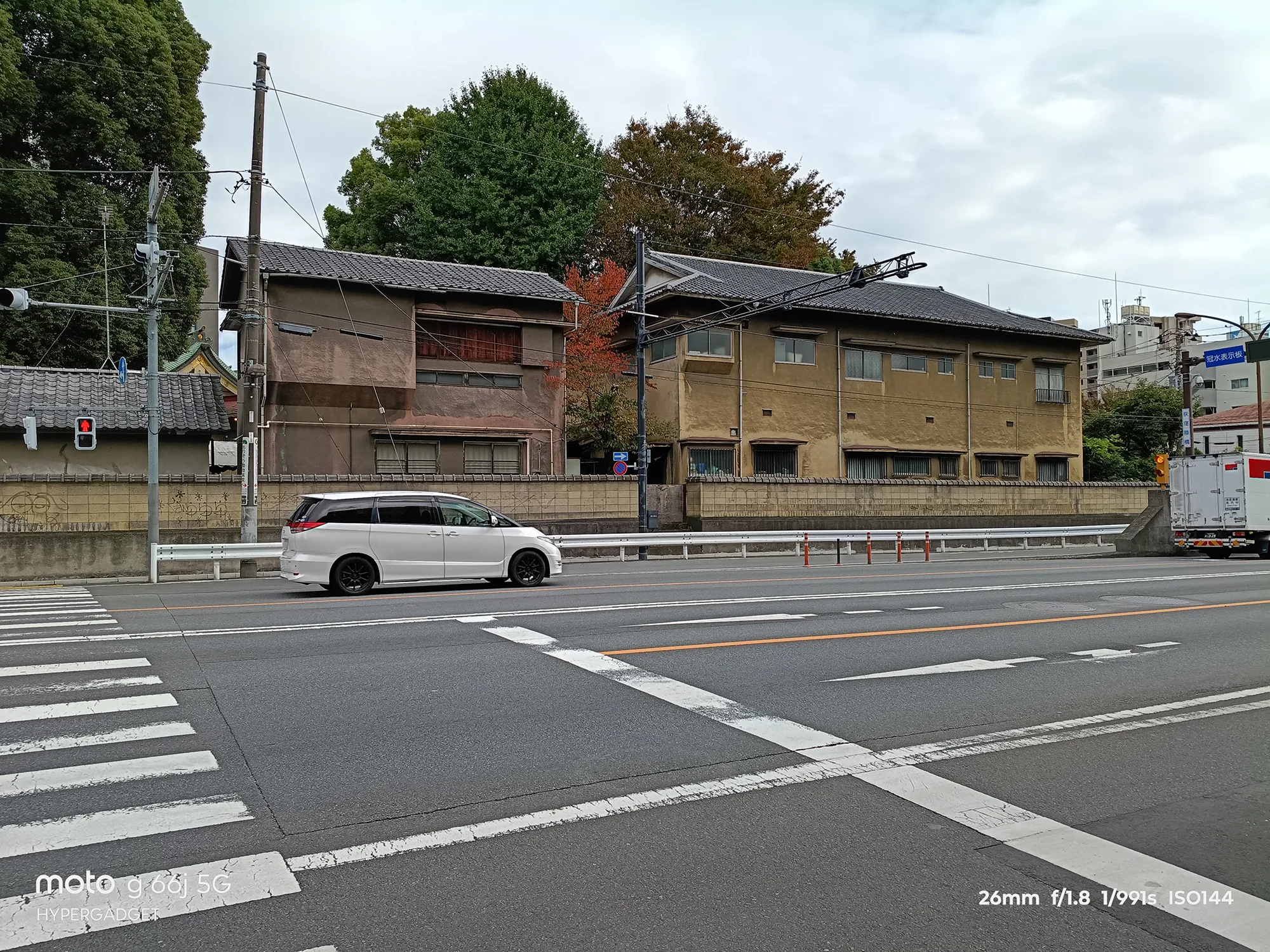 moto g66j 5Gのカメラ作例：紅葉が見える日本家屋と、横断歩道を横切る白い車を写した町並み写真
