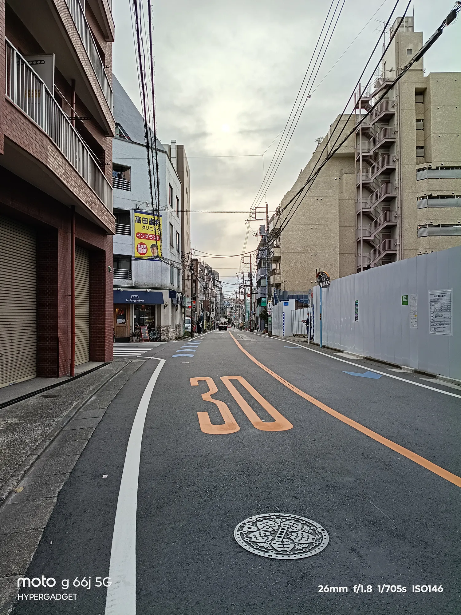 moto g66j 5Gのカメラ作例：路面に「30」と描かれた都市の狭い通り。奥へと続く道の遠近感と建物のディテールをレビュー