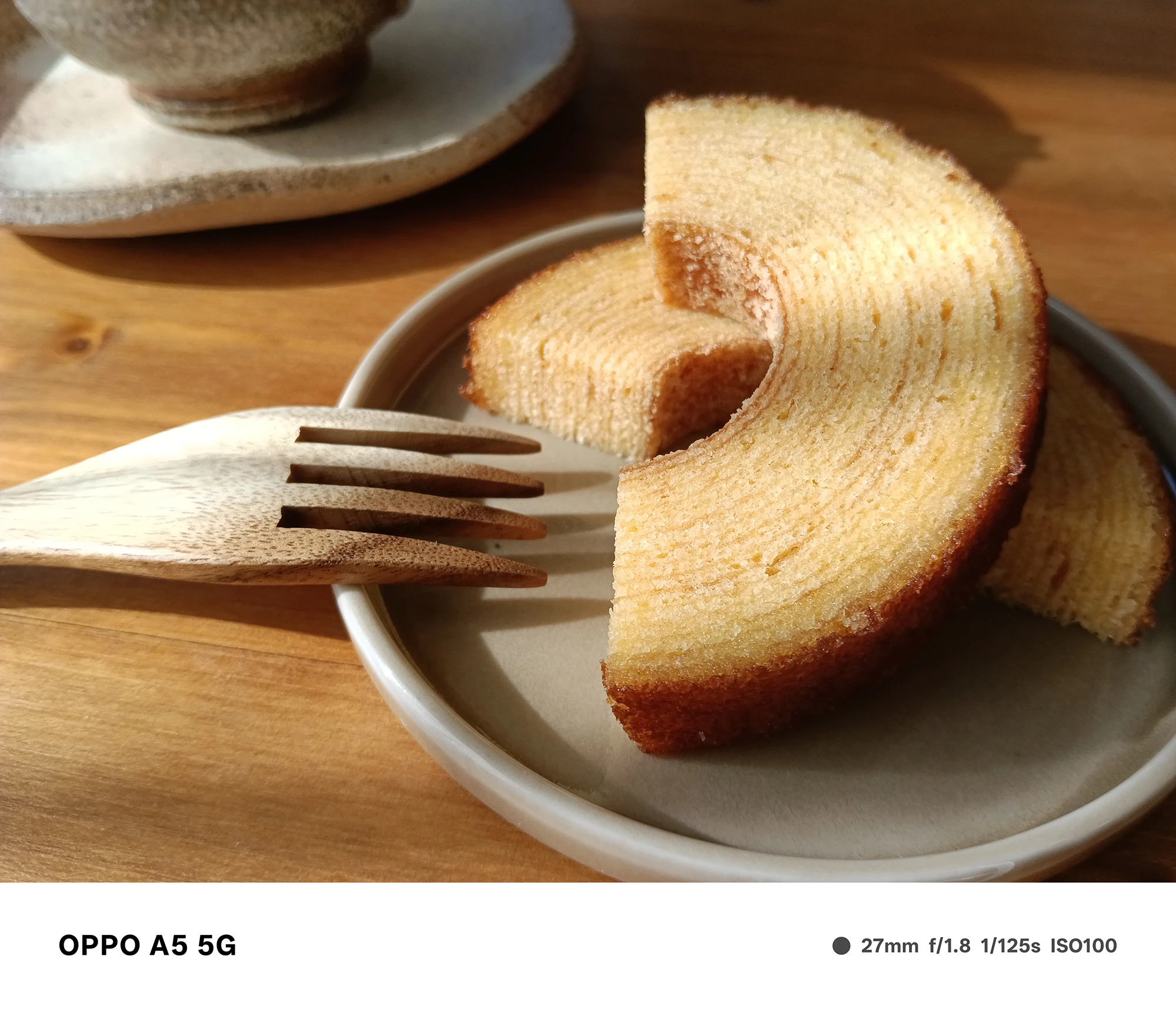 OPPO A5 5Gで撮影した皿に盛られたバウムクーヘン。木製フォークと柔らかな自然光が甘い質感を引き立てるテーブルフォト