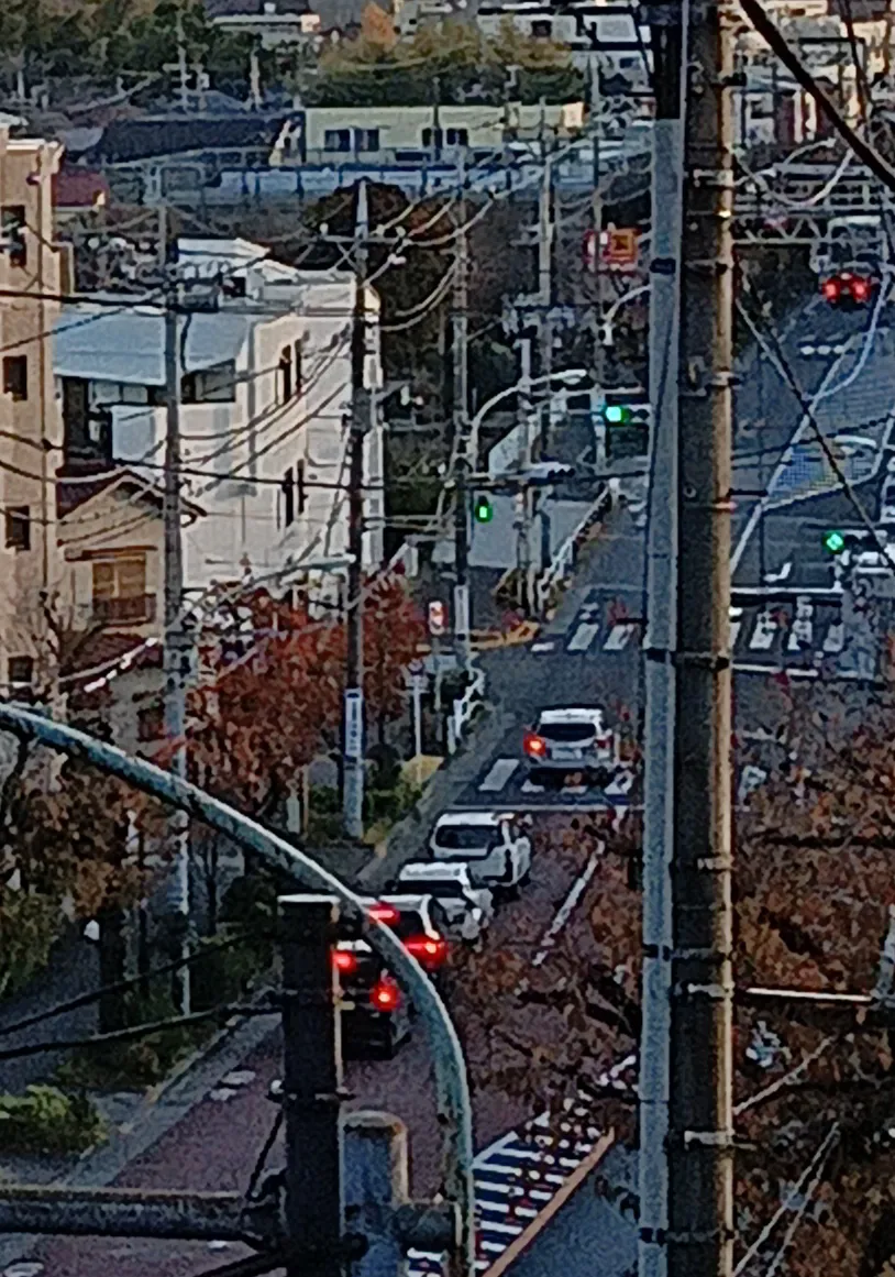 住宅街の道路を上から望み、車列と電柱が見える夕暮れ時の街並みの写真