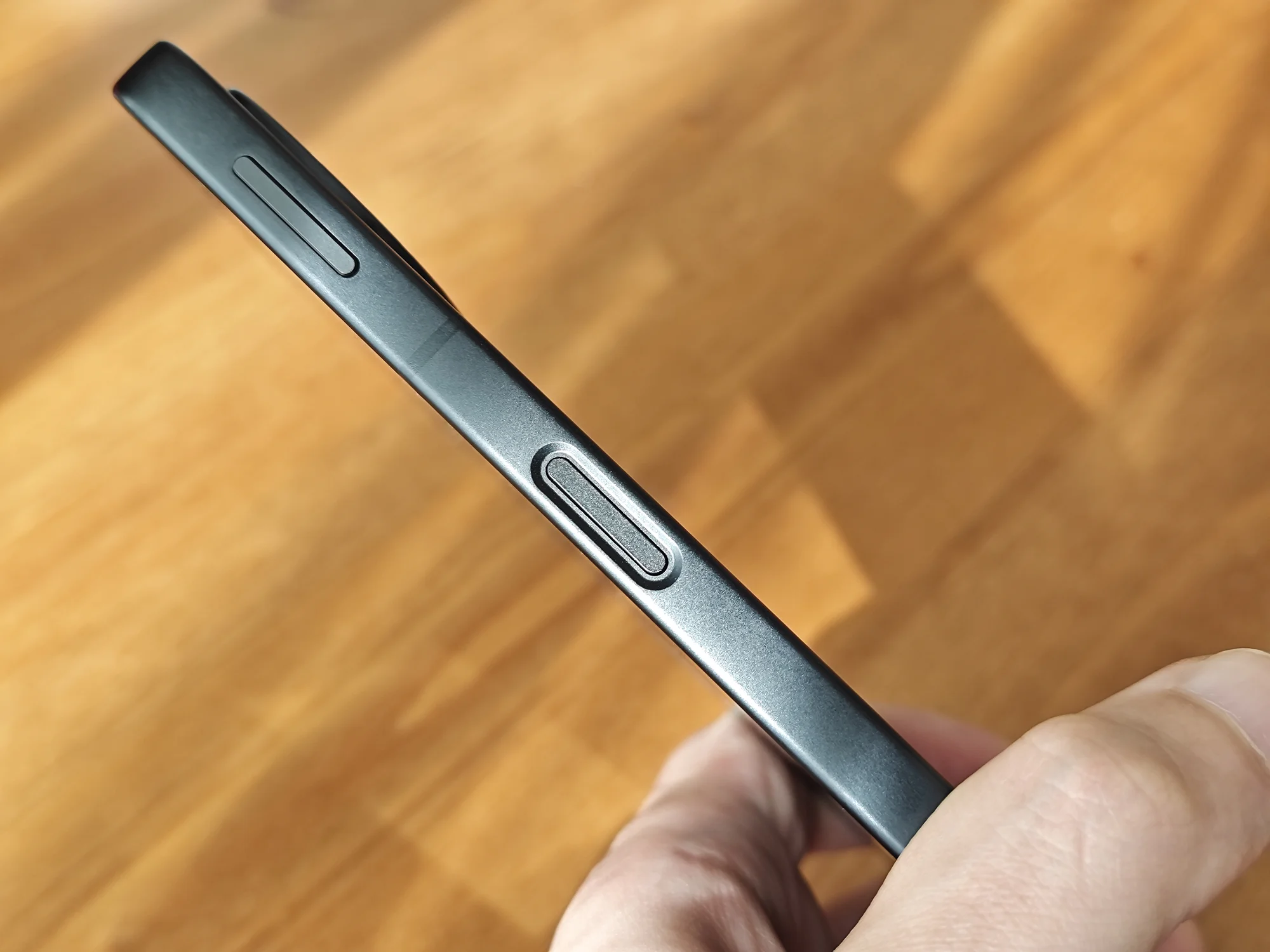 スマートフォンの側面（右サイド）をクローズアップした写真。上部に音量調整ボタン、中央に指紋認証センサー一体型の電源ボタンが見える。ボタン類はマットな質感で配置され、本体のデザインと操作性を示す。ボタン表面にはテクスチャ加工が施されている。