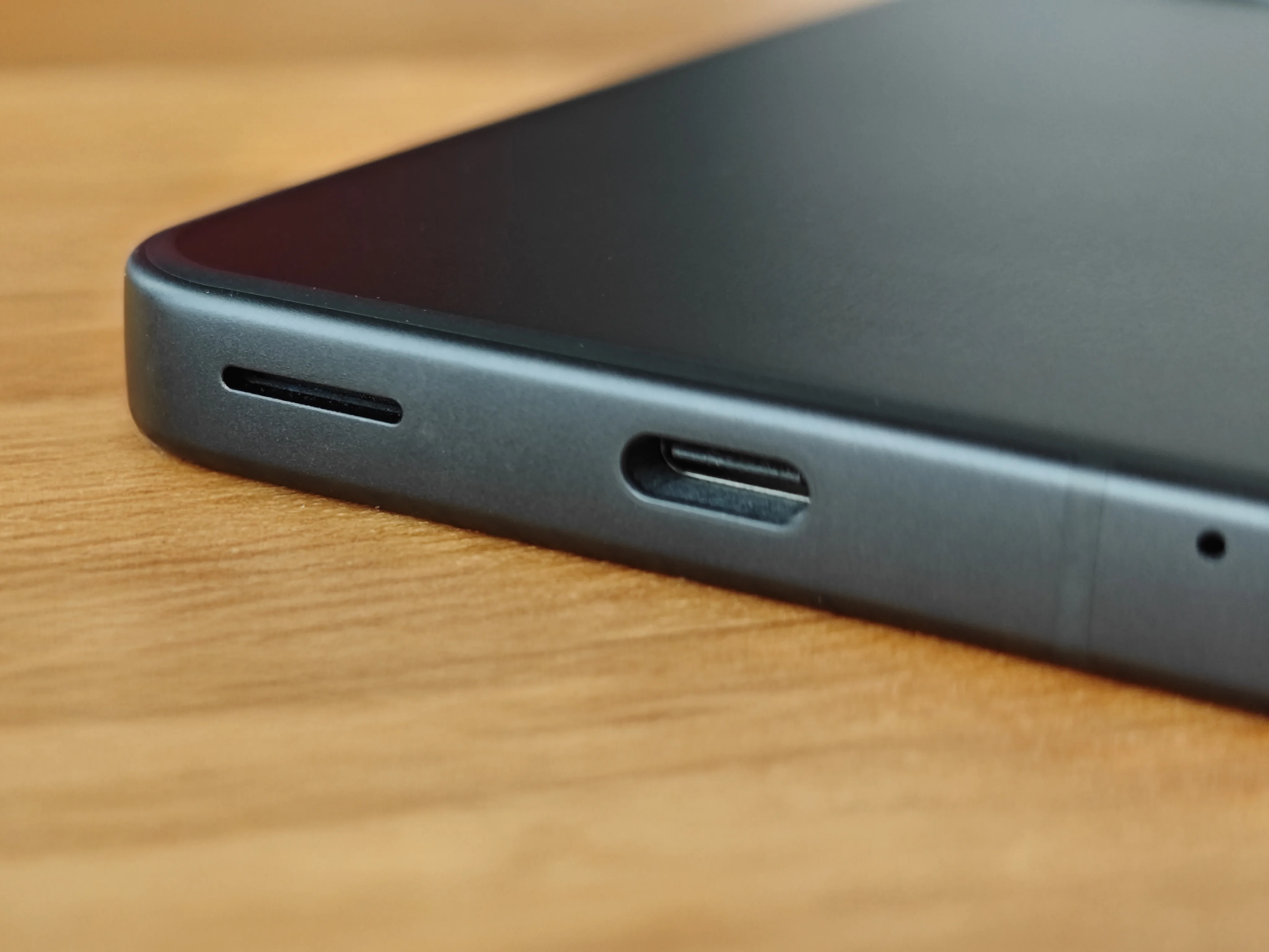 スマートフォンの底面を接写した写真。中央にUSB Type-Cポート、左側にスピーカーグリル、右端にマイク穴が配置されている。本体はマットな質感のブラックで、底面ポートの配置とデザインを示す。USB Type-Cポートによる充電およびデータ転送機能をアピール。