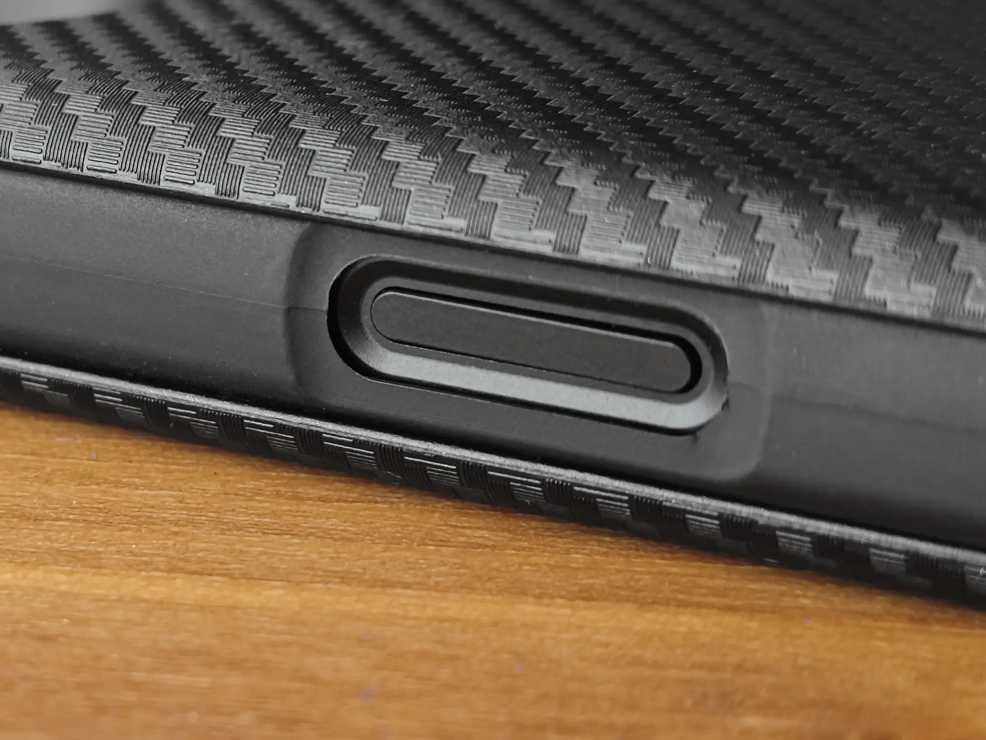 カーボンファイバー調のケースを装着したスマートフォンの側面を接写。ケースから露出している指紋認証センサー一体型の電源ボタンが見える。ボタン周りの加工が正確で、ケース装着時のボタンの押しやすさや指紋認証の利便性、高いフィット感をアピール。スマートフォンケースのレビューに関連。