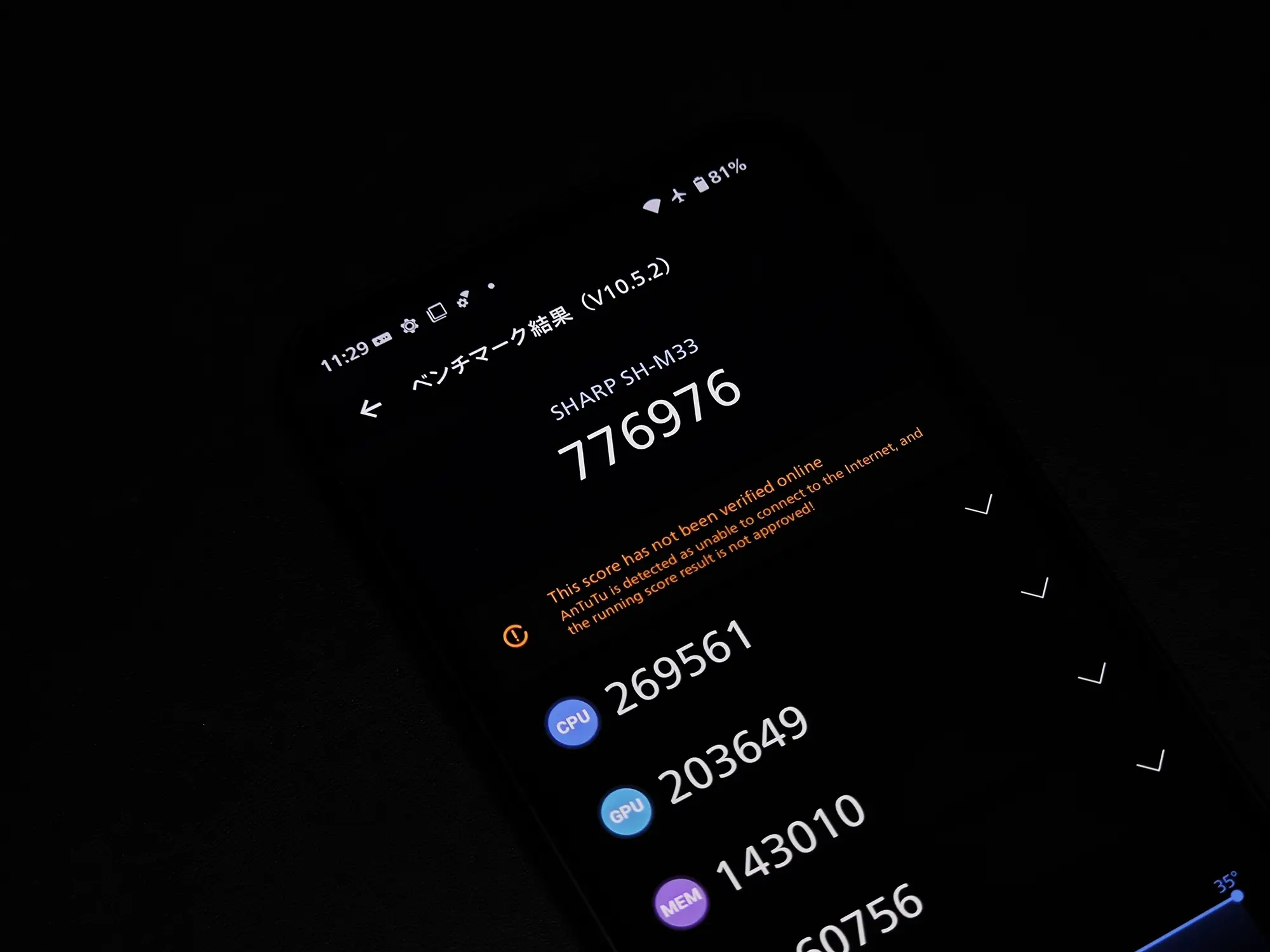 SHARP SH-M33のAnTuTuベンチマーク V10.5.2結果を映したスマートフォンの画面。総合スコアは776,976点で、CPU 269,561点、GPU 203,649点。画面は暗所で撮影されており、有機ELディスプレイの黒の締まりと、高いミッドレンジ性能を同時にアピール。