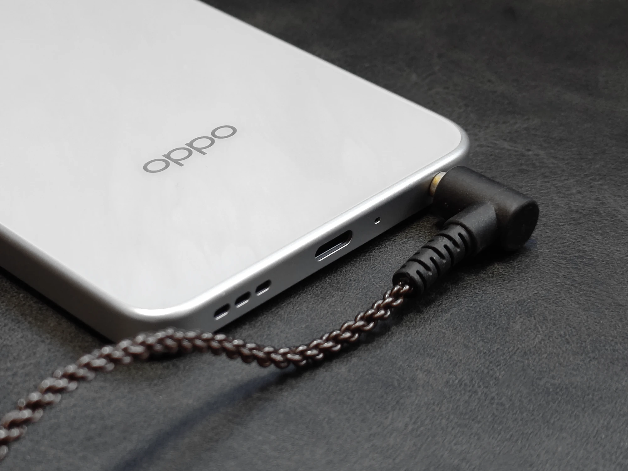 OPPO A5 5Gの底面クローズアップ。3.5mmイヤホンジャックにL字型のプラグの有線イヤホンが接続されており、USB Type-Cポートとスピーカー穴も見える。