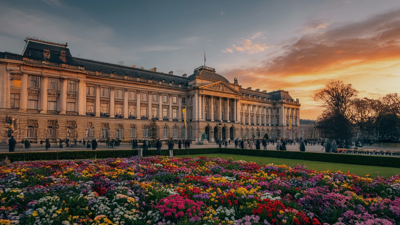 宮殿を正面から捉え、手前に色鮮やかな花が敷き詰められた風景。夕日が雲を照らし、温かい色に包まれた情景。