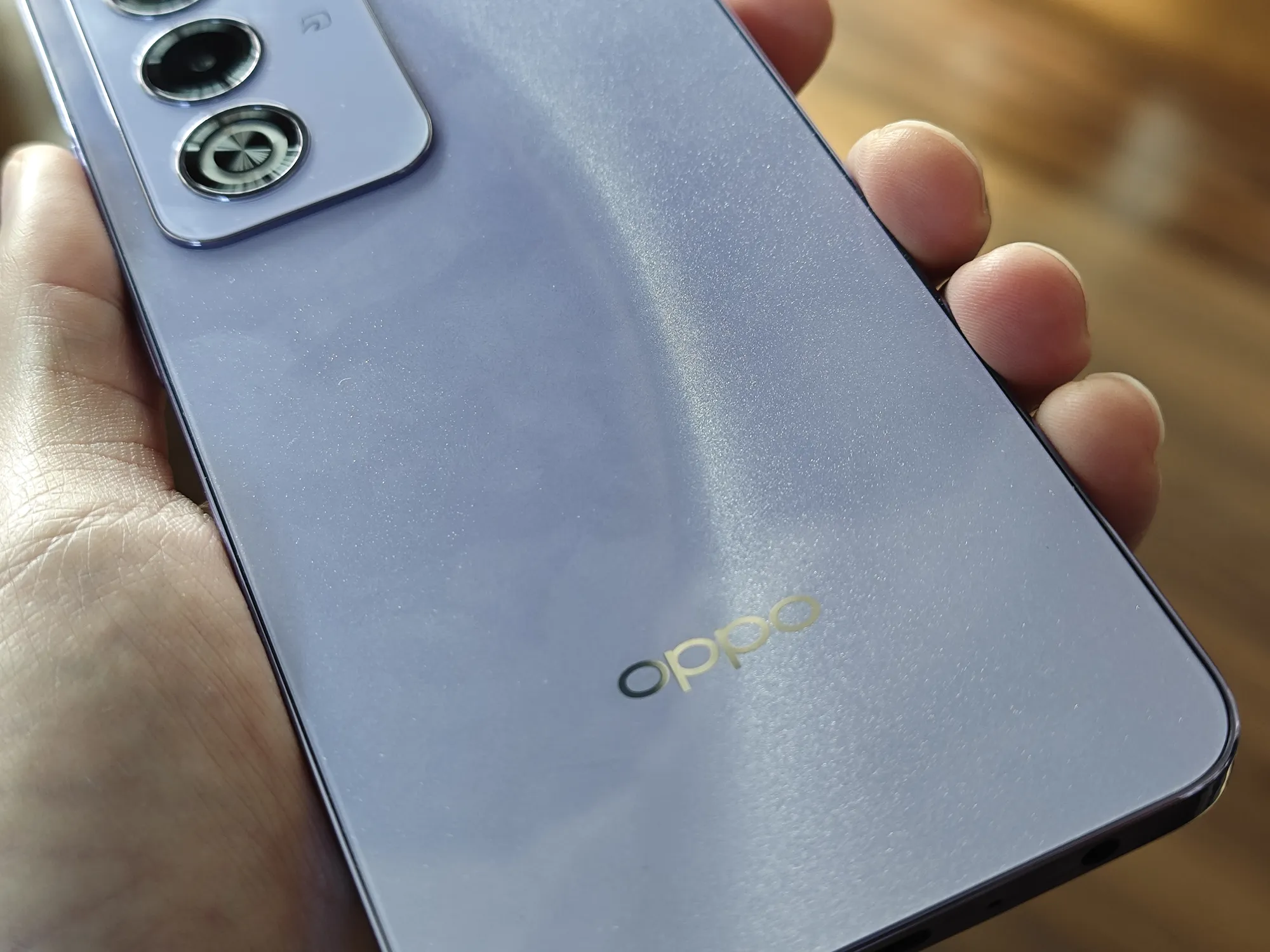 手に持たれた光沢のあるパープル系のOPPOスマートフォンの背面。上部にはトリプルカメラユニットがあり、中央下部にはゴールドのOPPOロゴが配置されている。