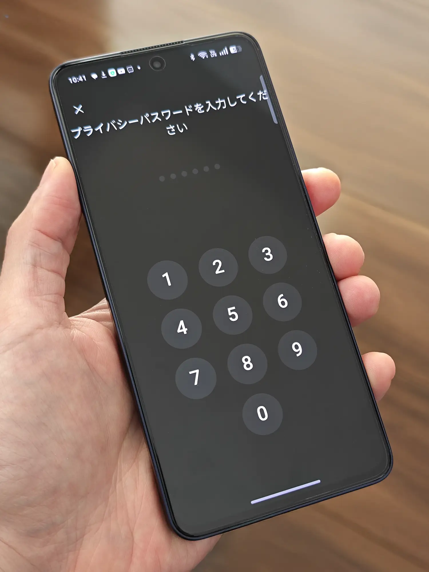 OPPO Reno13 Aを手に持ち、アプリロックやプライバシー保護のための「プライバシーパスワードを入力してください」という画面が表示されている様子。画面中央には数字入力用のテンキーが表示されている