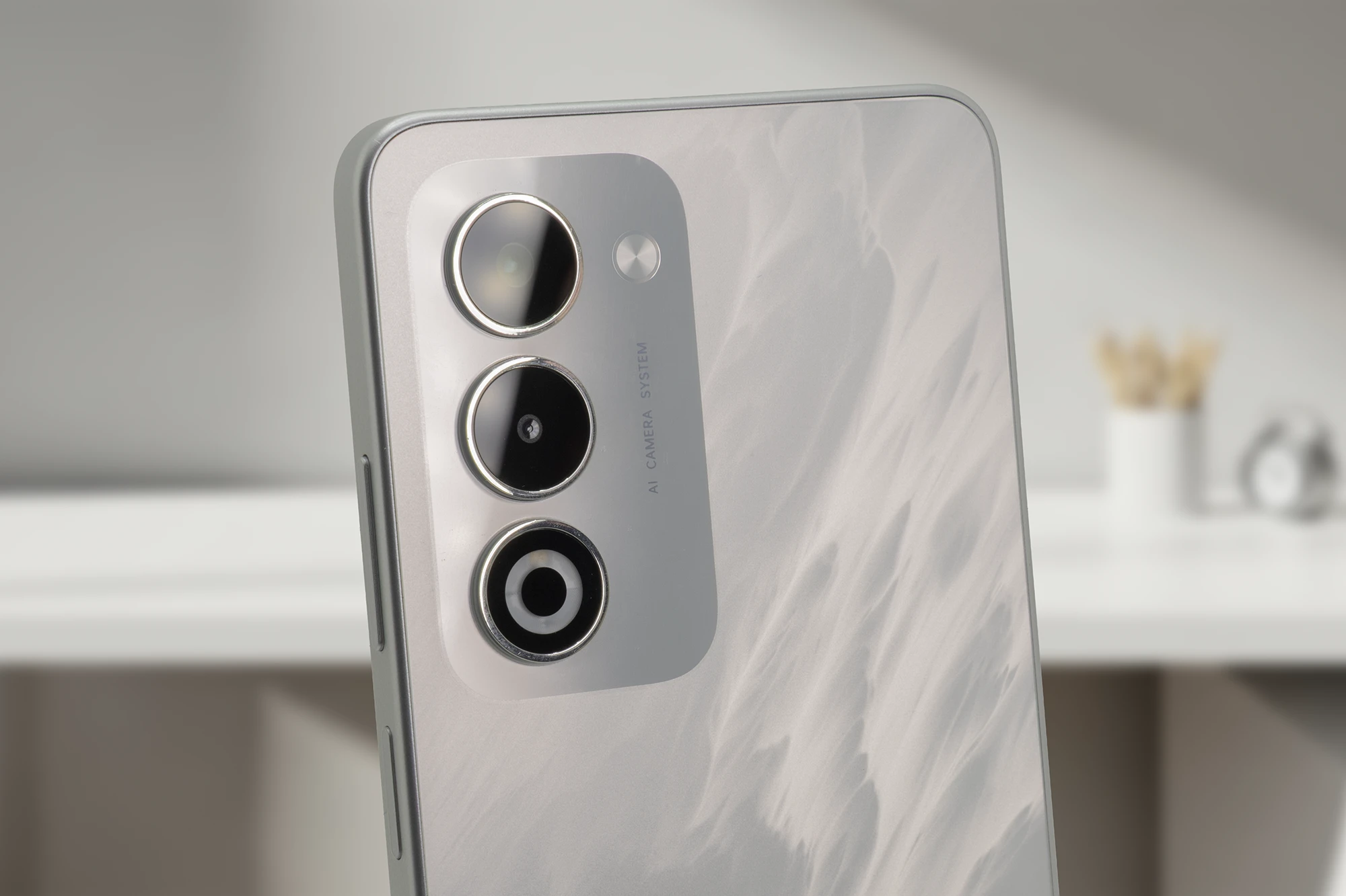 OPPO A5 5Gのホワイトの背面を接写。縦に並んだトリプルカメラユニットと、その横に「AI CAMERA SYSTEM」の文字が見える。背面パネルには光沢のある特殊な波紋状のテクスチャが施されており、高性能AIトリプルカメラと洗練されたデザインをアピール。