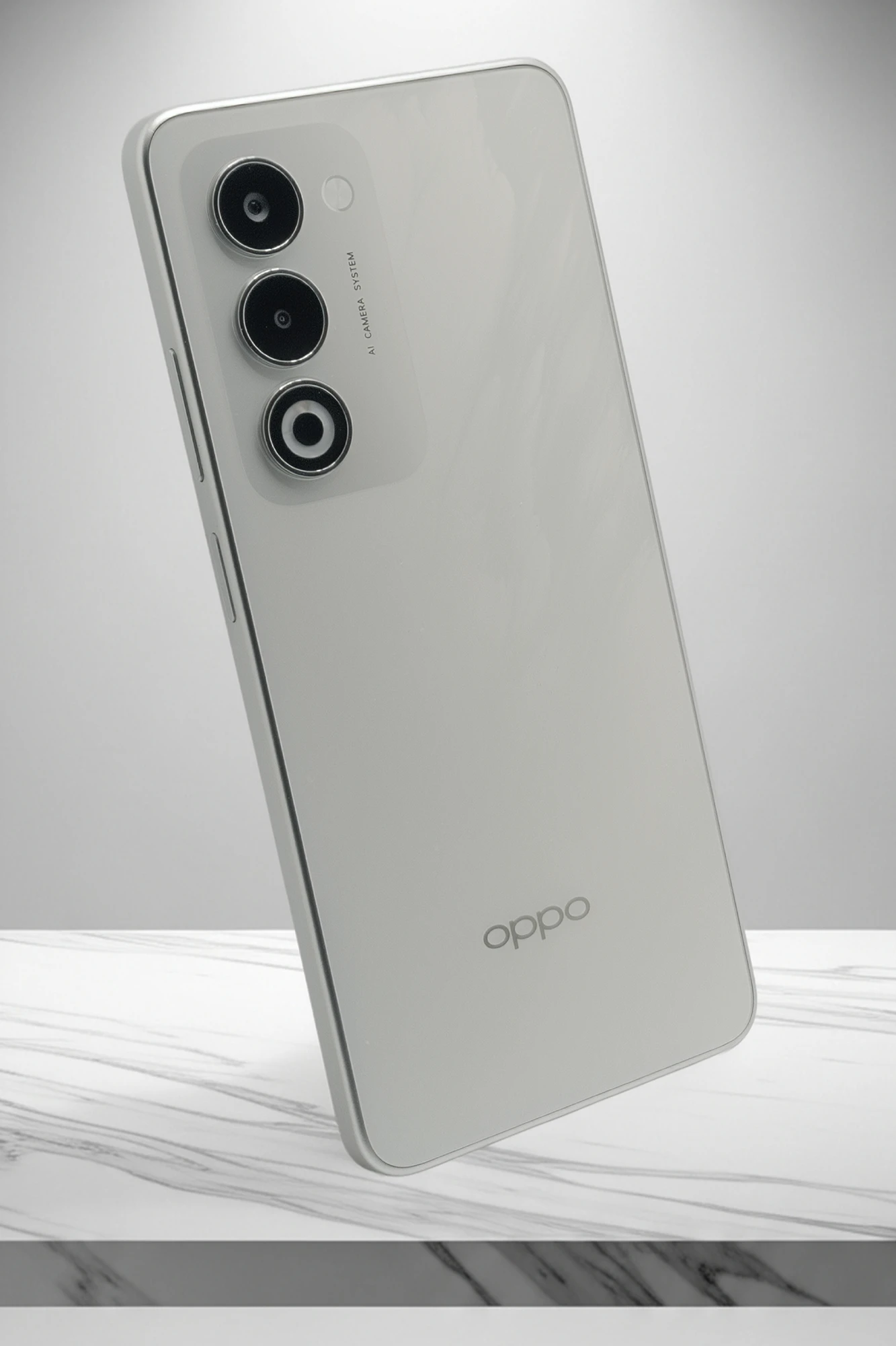 ホワイトまたはシルバーのシンプルな背面デザインのOPPO A5 5G。垂直に配置されたトリプルカメラユニットと「AI CAMERA SYSTEM」の刻印、下部にOPPOロゴがある。