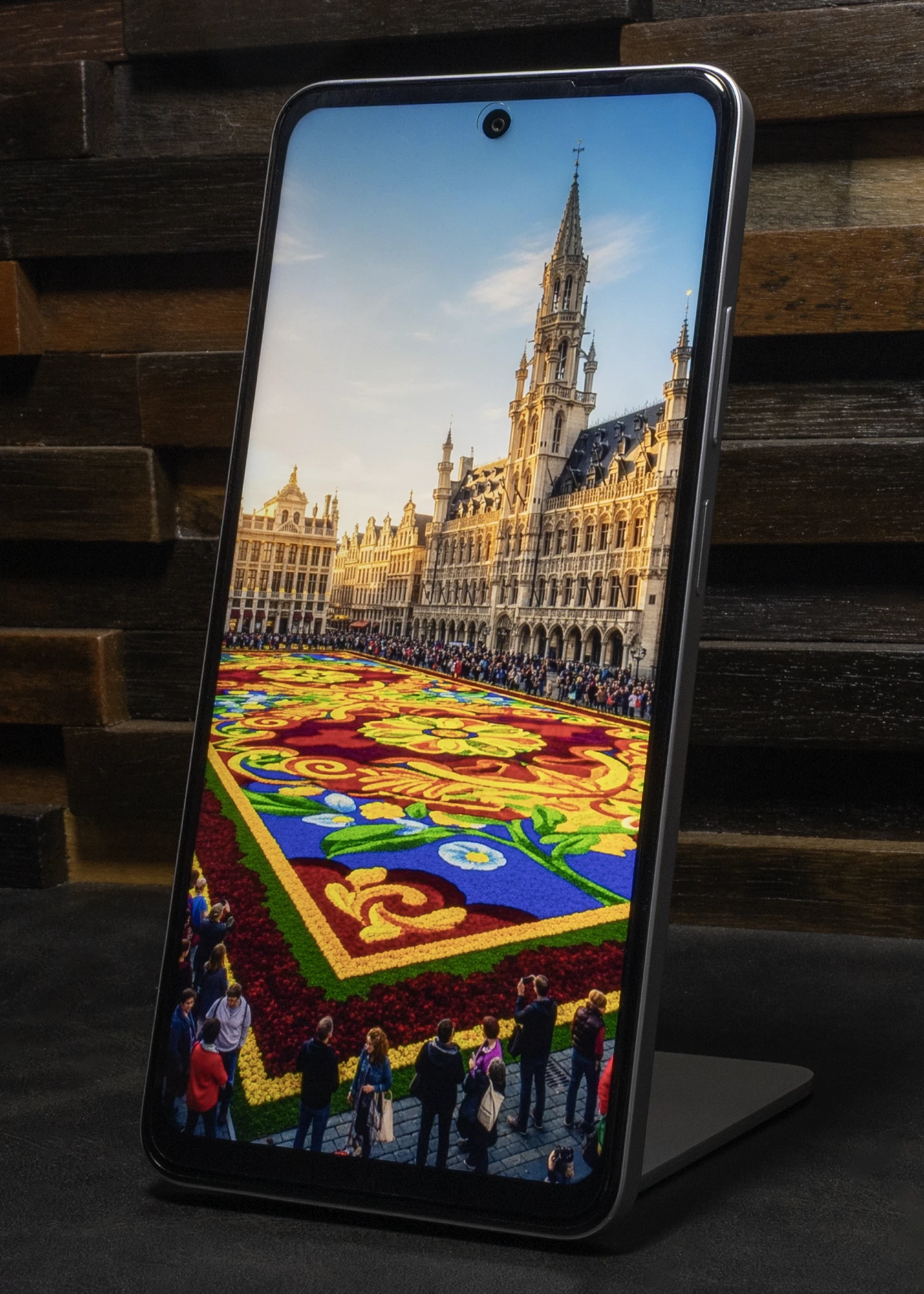 スタンドに立てられたOPPO A5 5Gのディスプレイに、ベルギーのグラン・プラスの市庁舎と広場いっぱいに敷き詰められた花の絨毯の鮮やかな写真が表示されている。上部中央にはパンチホールカメラが見える。