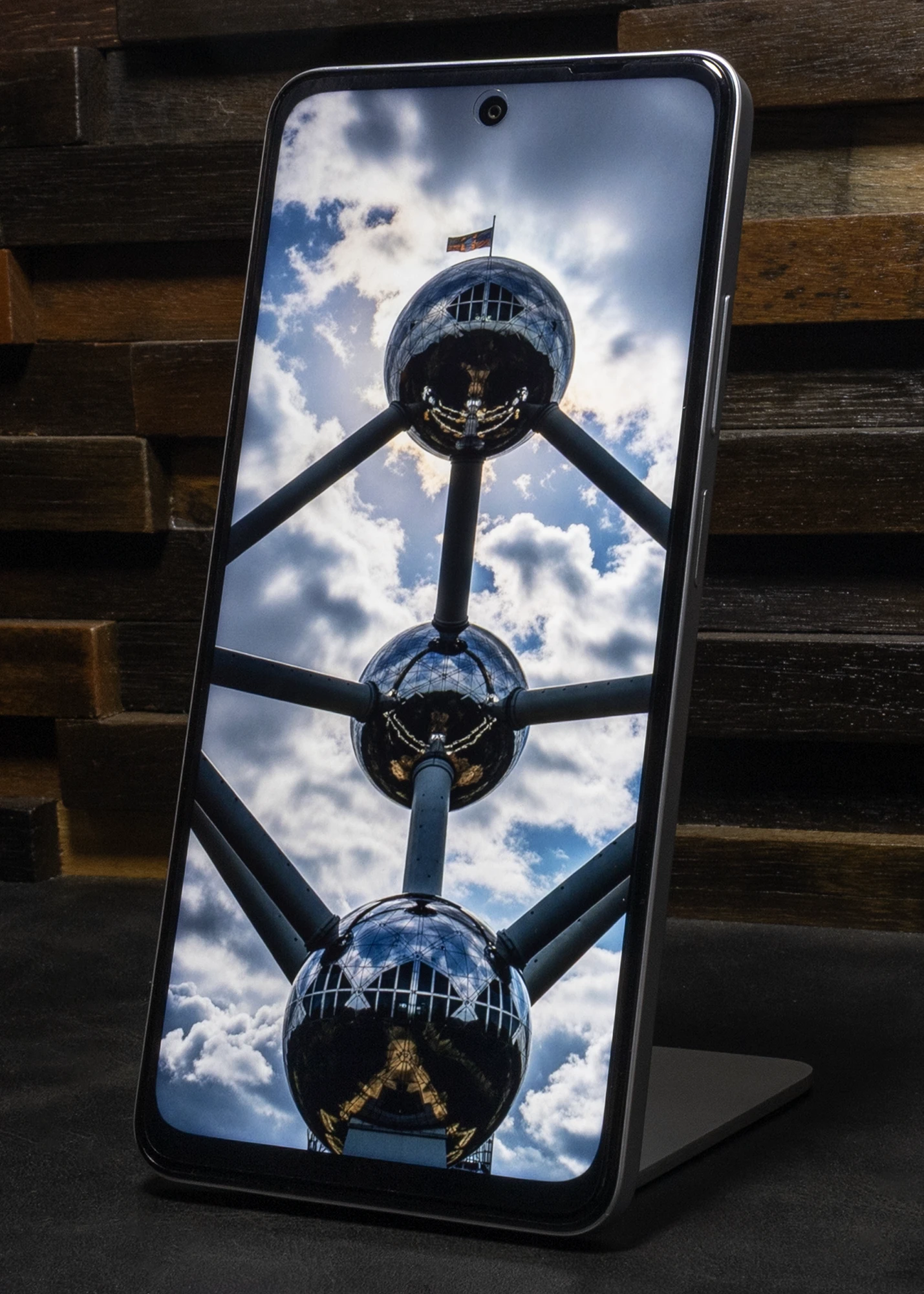 スタンドに立てられたOPPO A5 5Gのディスプレイに、曇り空を背景にしたアトミウムのダイナミックな写真が表示されている。ディスプレイ上部中央にはパンチホールカメラが見える。