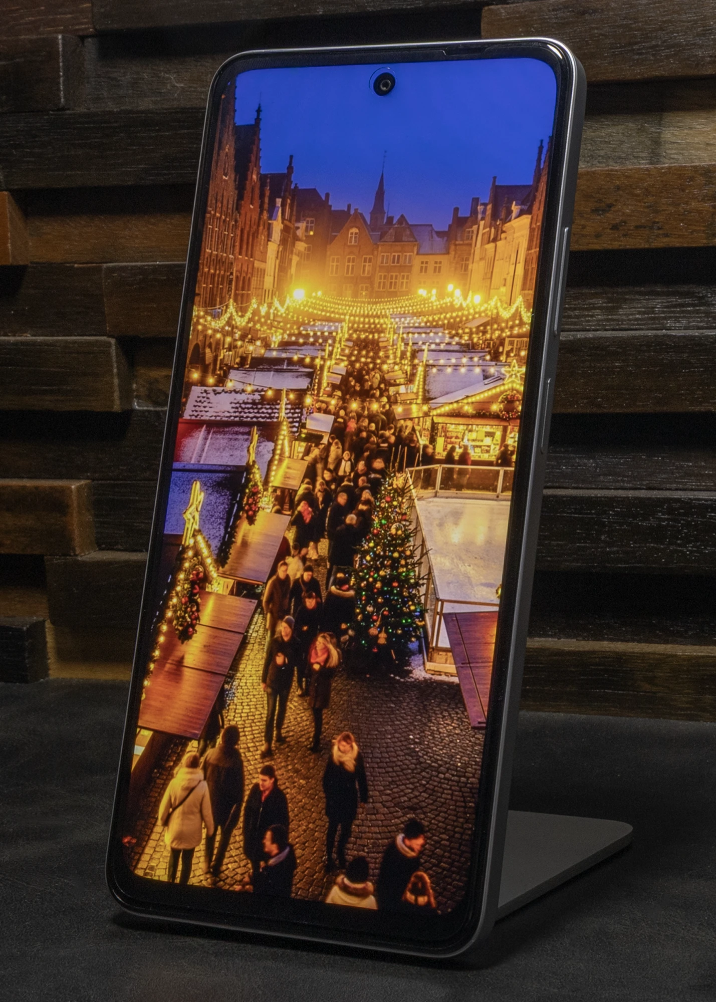 スタンドに立てられたOPPO A5 5Gのディスプレイに、クリスマスツリーとマーケットの屋台が並ぶ、温かい光に照らされた夜のヨーロッパの街並みの写真が表示されている。上部中央にはパンチホールカメラが見える。