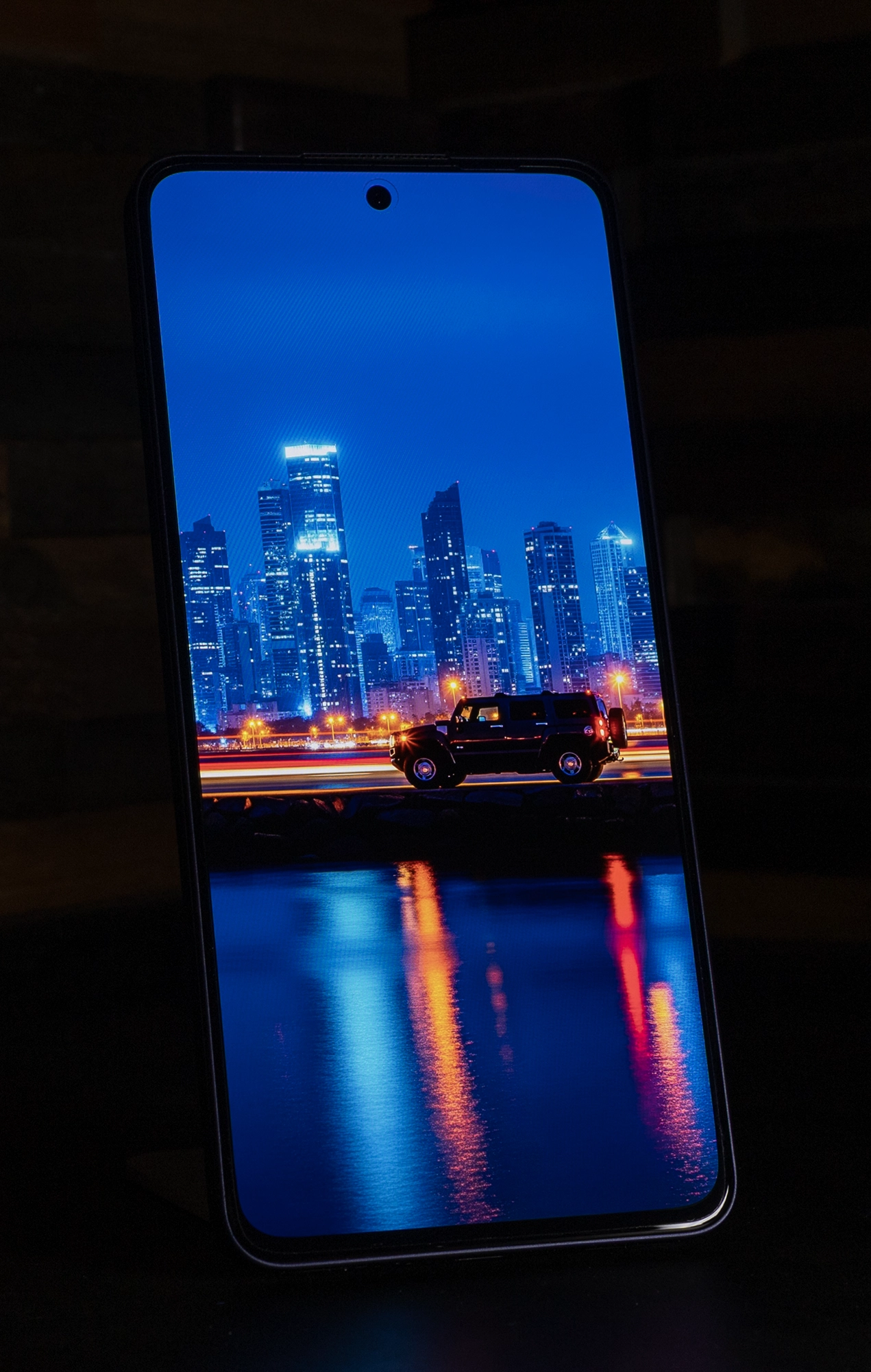 OPPO Reno13 Aのディスプレイに映し出された、夜の都市のスカイラインを背景に走る車の画像