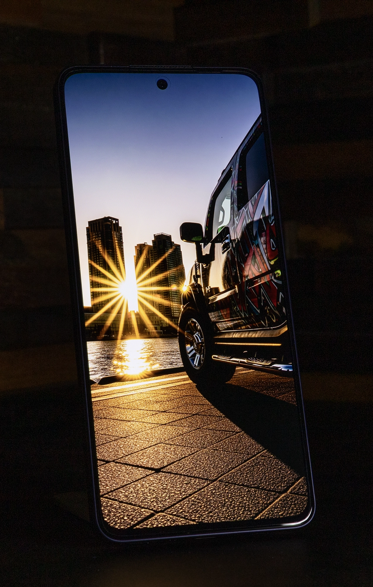 OPPO Reno13 Aのディスプレイに映し出された、夕日の光条と高層ビルを背にした車の画像