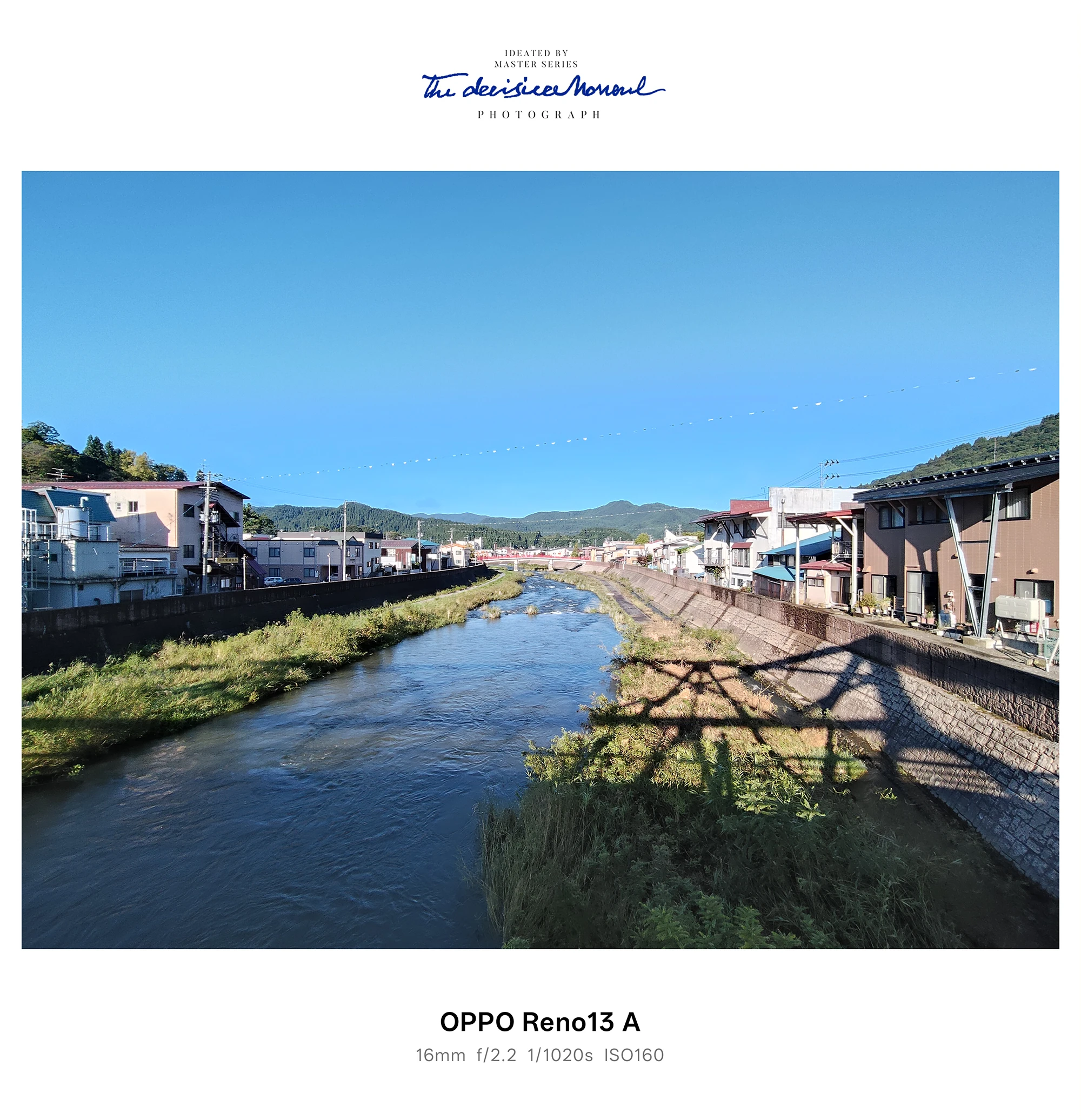 OPPO Reno13 Aの超広角で撮影した川沿いの街並みと青空（橋の影が水面に映る）