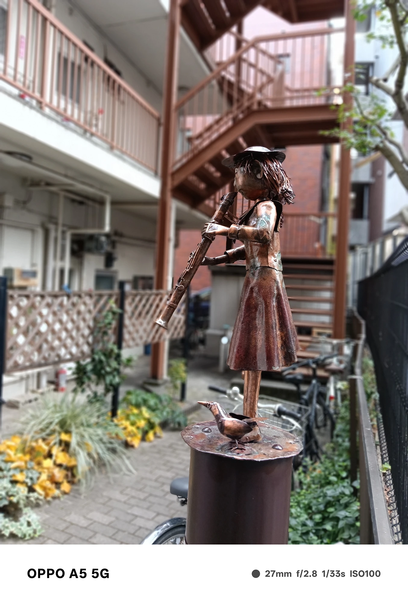 OPPO A5 5Gで撮影したフルートを持つ少女の金属像の接写。背景が滑らかにぼけ、被写体の質感が際立つポートレート風作例