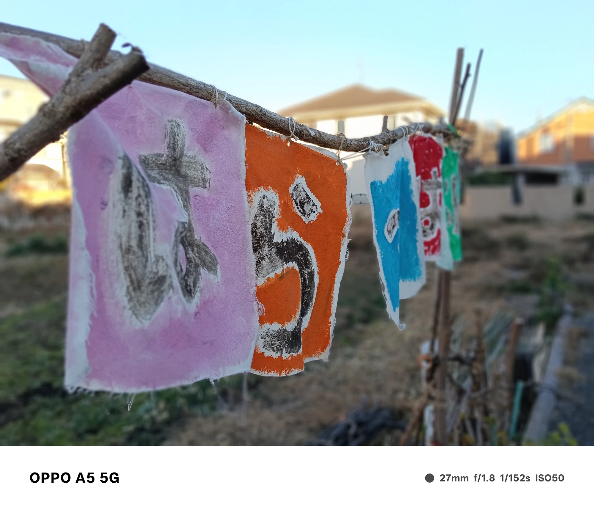 OPPO A5 5Gで撮影したカラフルな手作りの旗。『は』の文字が描かれた布を主題に、背景の住宅地を柔らかくぼかした構図