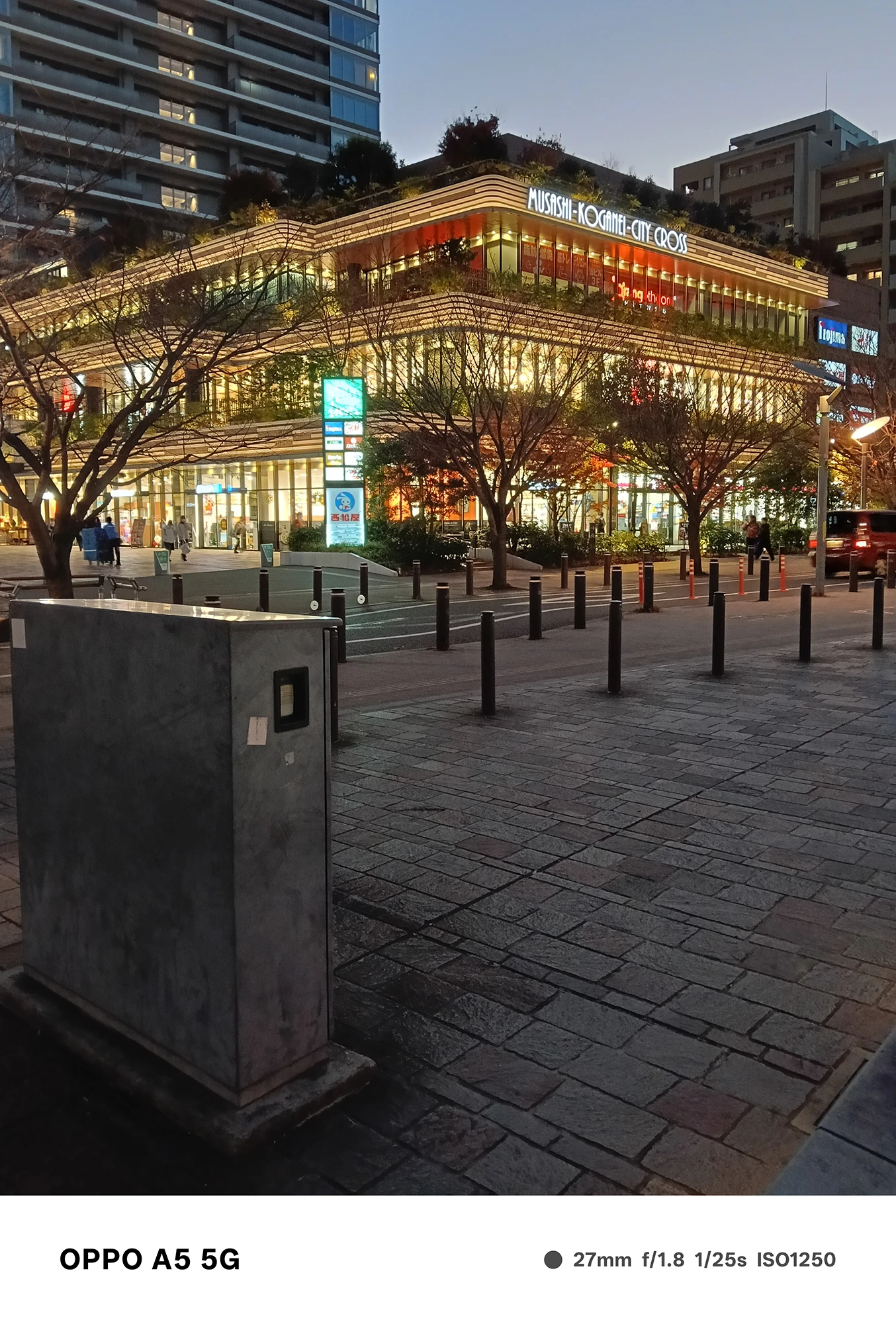 OPPO A5 5Gで撮影した武蔵小金井駅前の商業ビル。夕暮れ時に建物のライトが点灯し、街路樹のシルエットと反射光が美しく描写された夜景