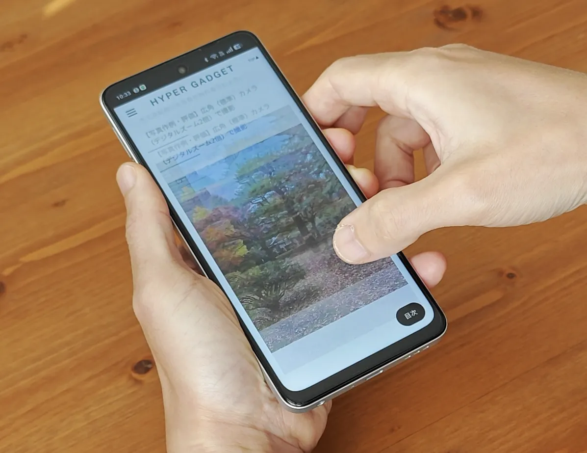 両手で持たれたOPPO A5 5Gでウェブページ(HYPER GADGET)が表示されており、親指で画面をスクロールしている様子。画面上部にはパンチホールカメラが見える。