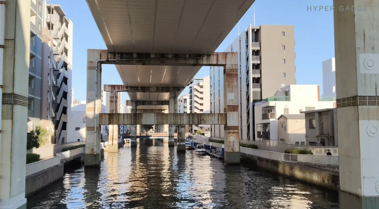 OPPO Reno13 A 昼景作例：高架下の水路と建築群を直線構図で撮影（逆光耐性検証）