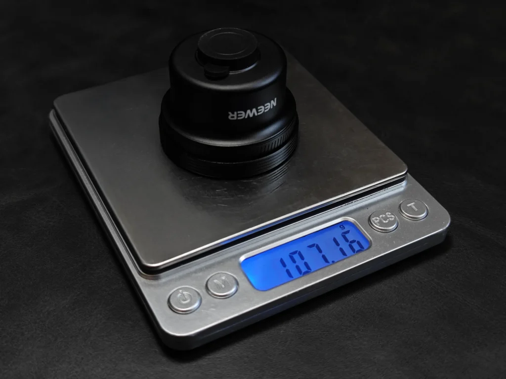 デジタル秤で計測したNEEWER LS-71 58mm望遠レンズ単体の重量（約107.16g）。レンズの軽量性を確認。