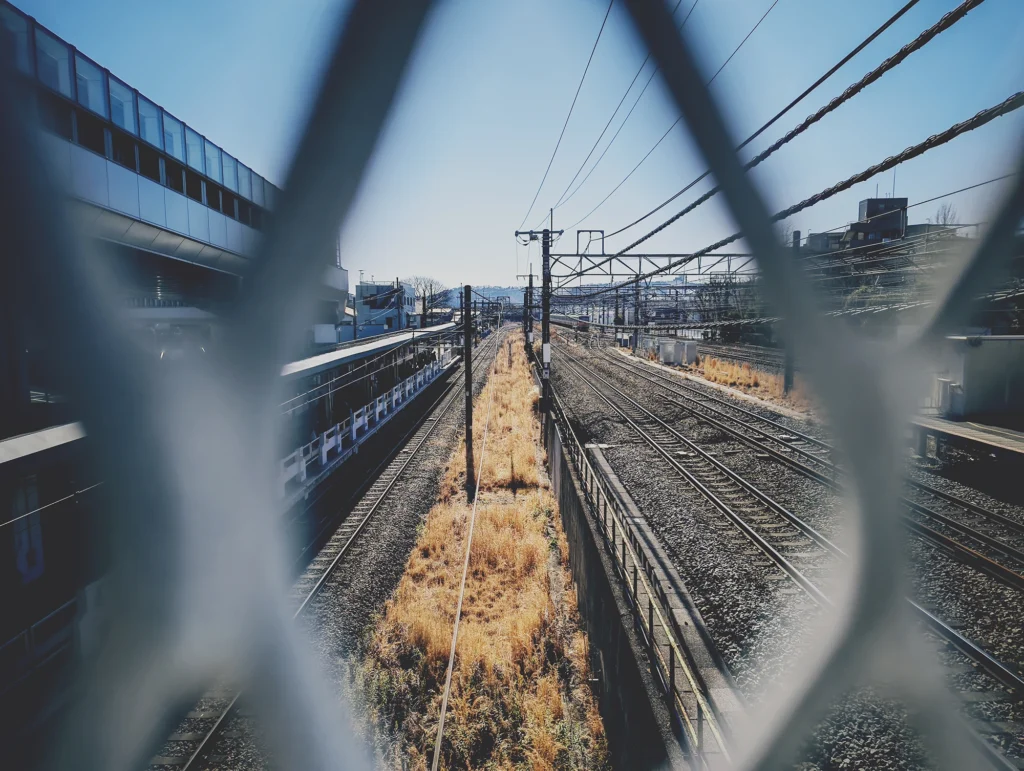 Nothing Phone (3a) Liteの作例。金網から線路と走ってくる電車を撮影し、フィルム風LUTでノスタルジックに仕上げた写真