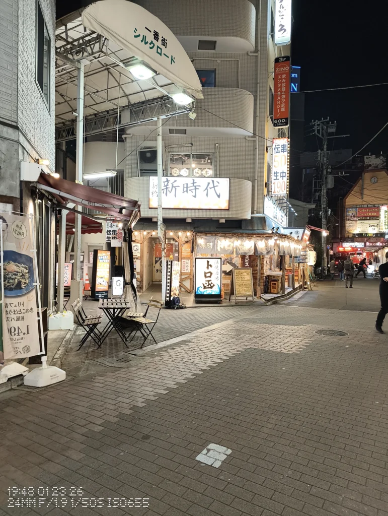 Nothing Phone (3a) Lite/カメラ:メイン(広角)/焦点距離:24mm相当/内容:アーケード入口と発光看板が並ぶ夜の商店街、街灯と看板光で路面まで明るい通り。