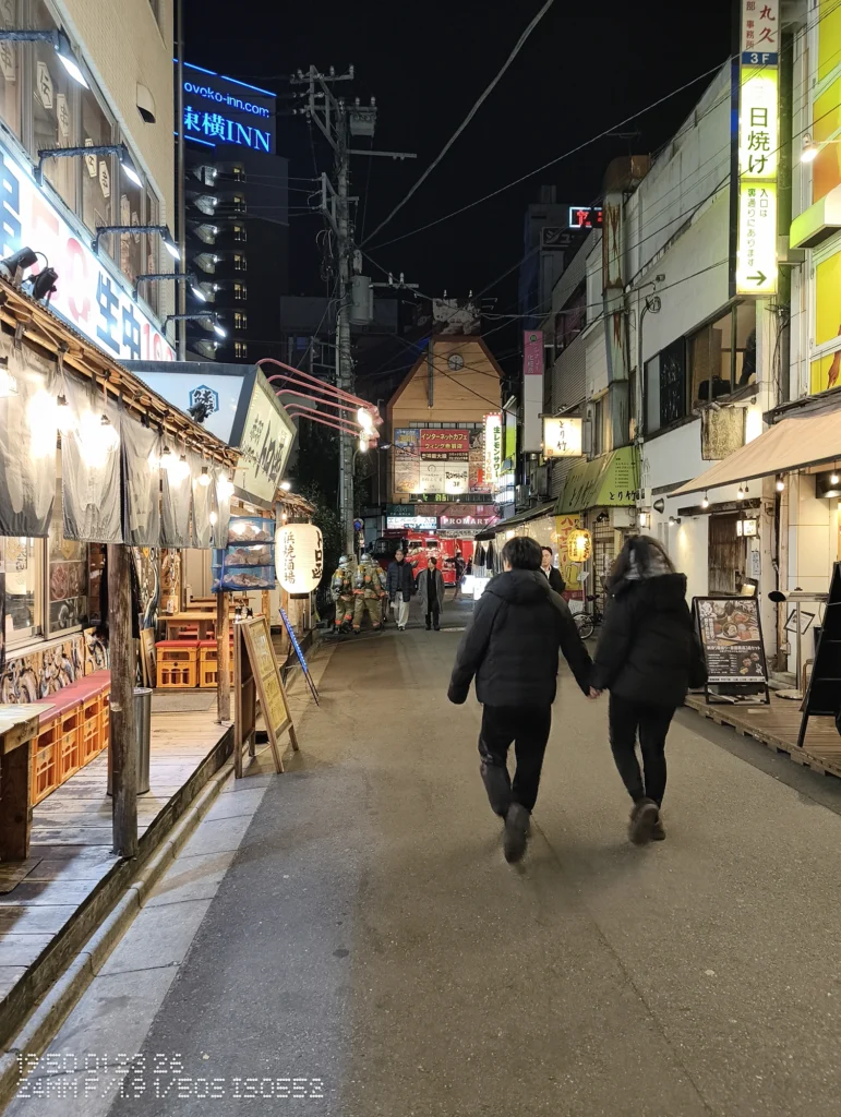 Nothing Phone (3a) Lite/カメラ:メイン(広角)/焦点距離:24mm相当/内容:飲食店の灯りと看板が続く夜の路地、手をつないで歩く人と遠景のネオンが見える通り。
