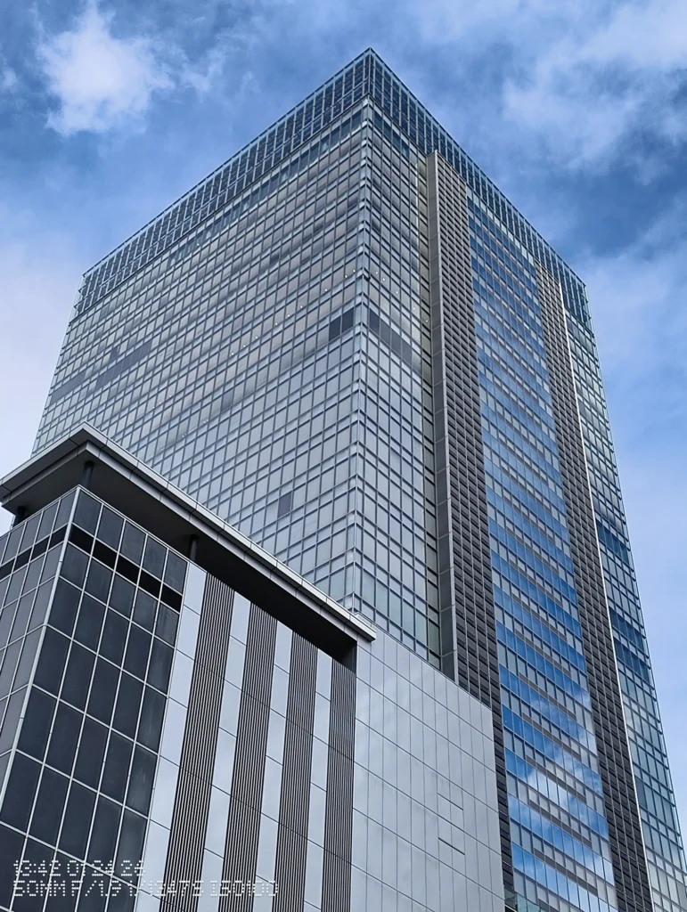 Nothing Phone (3a) Lite/カメラ:メイン(広角)2倍ズーム/焦点距離:50mm相当/内容:ガラス外装の高層ビルを見上げ、窓の格子が細かく並ぶ様子を捉えた日中屋外の2倍ズーム作例