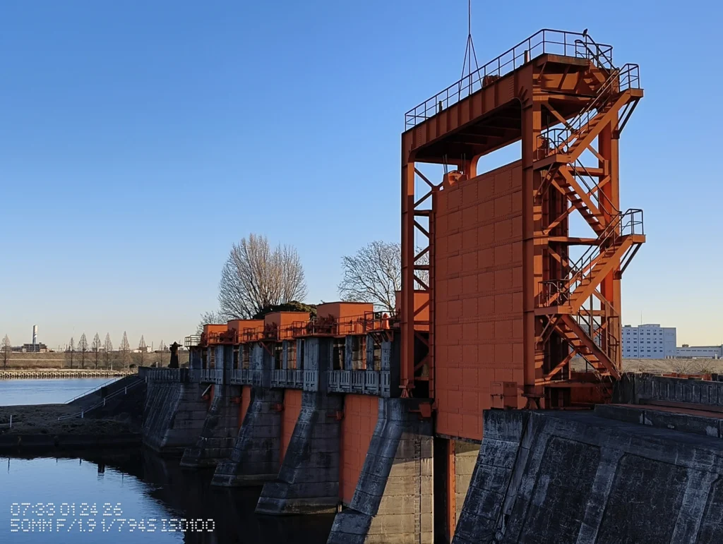 Nothing Phone (3a) Lite/カメラ:メイン(広角)2倍ズーム/焦点距離:50mm相当/内容:川沿いの大型水門(鉄骨階段付き)を青空背景で切り取った屋外の2倍ズーム作例