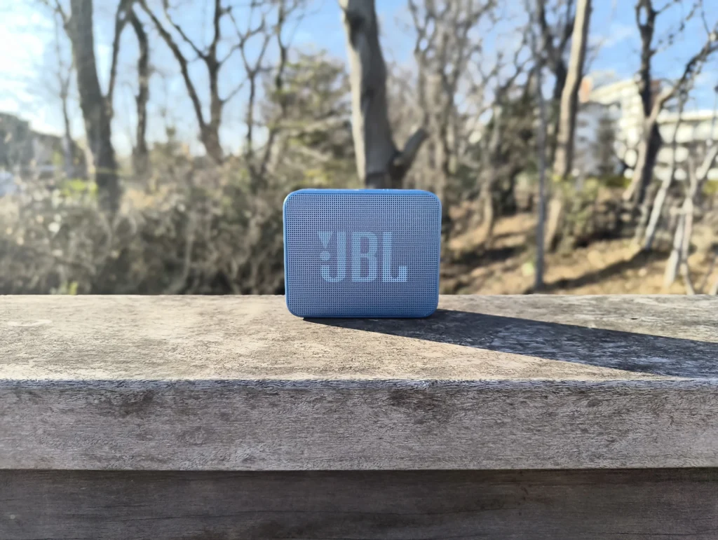 端末名:Nothing Phone (3a) Lite/カメラ:メイン(広角)ポートレート/焦点距離:確認不能(mm相当)mm相当/内容:木柵の上の青いスピーカーを主題に背景ボケで冬木立を整理した昼のポートレート、シンプルで抜けの良い雰囲気